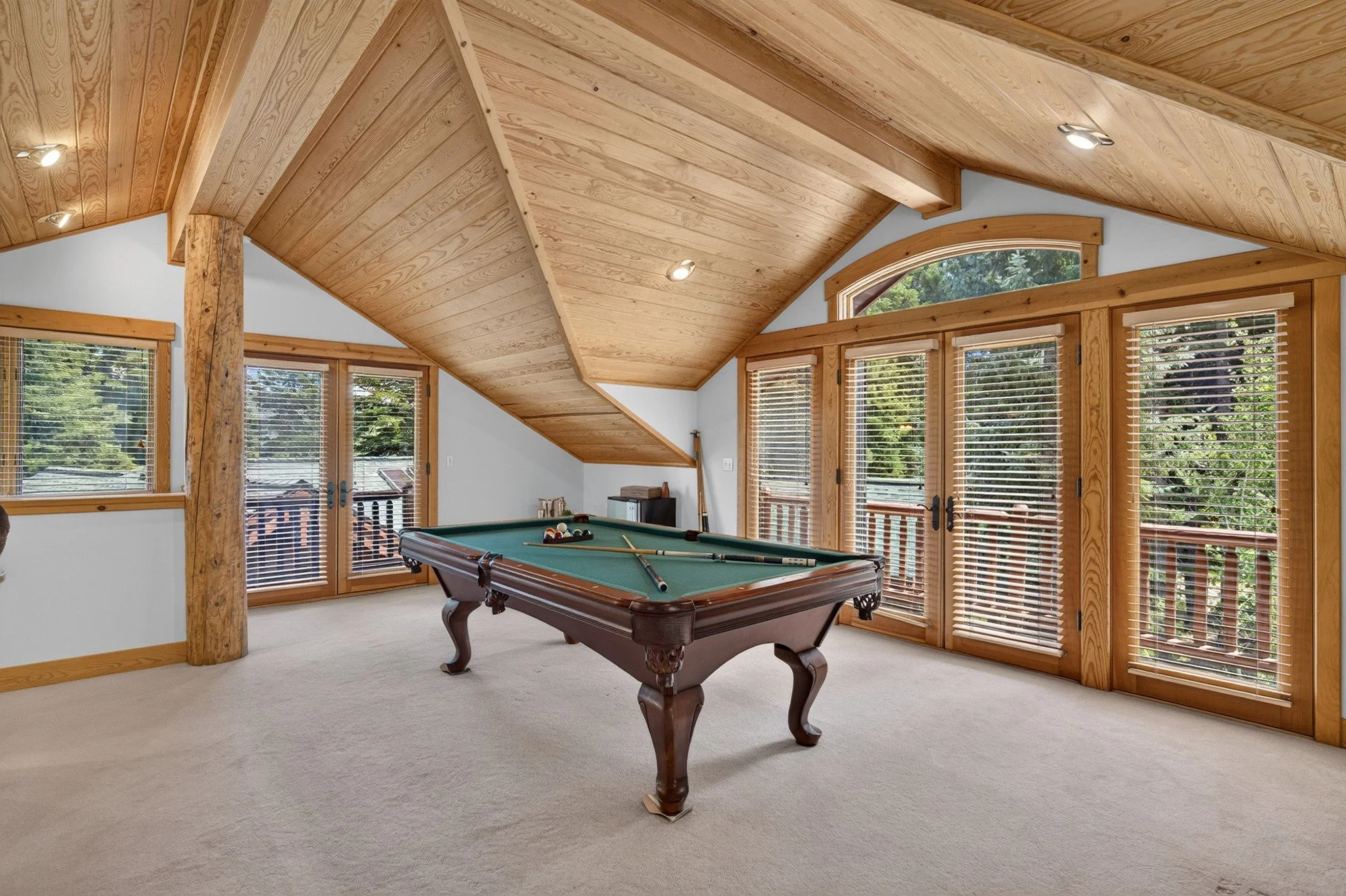 Recreation room with a pool table under a vaulted wood ceiling with exposed beams and tall windows to the trees