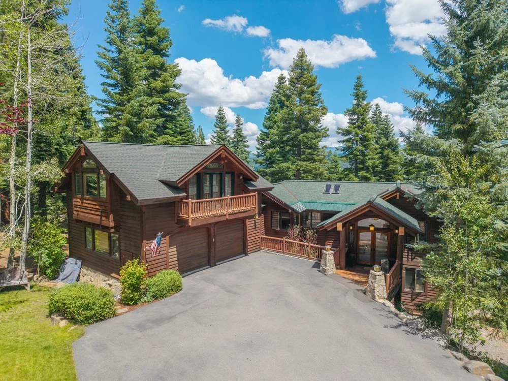 Exterior view of 2211 Silver Fox Court surrounded by mature evergreen trees under a blue sky.