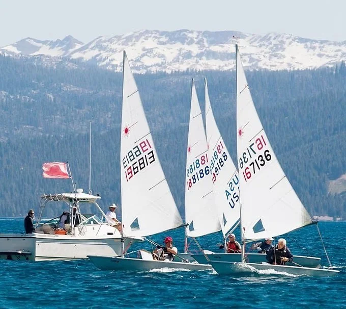 Laser and ILCA dinghies racing on Lake Tahoe with snow-covered Sierra mountains in the background.