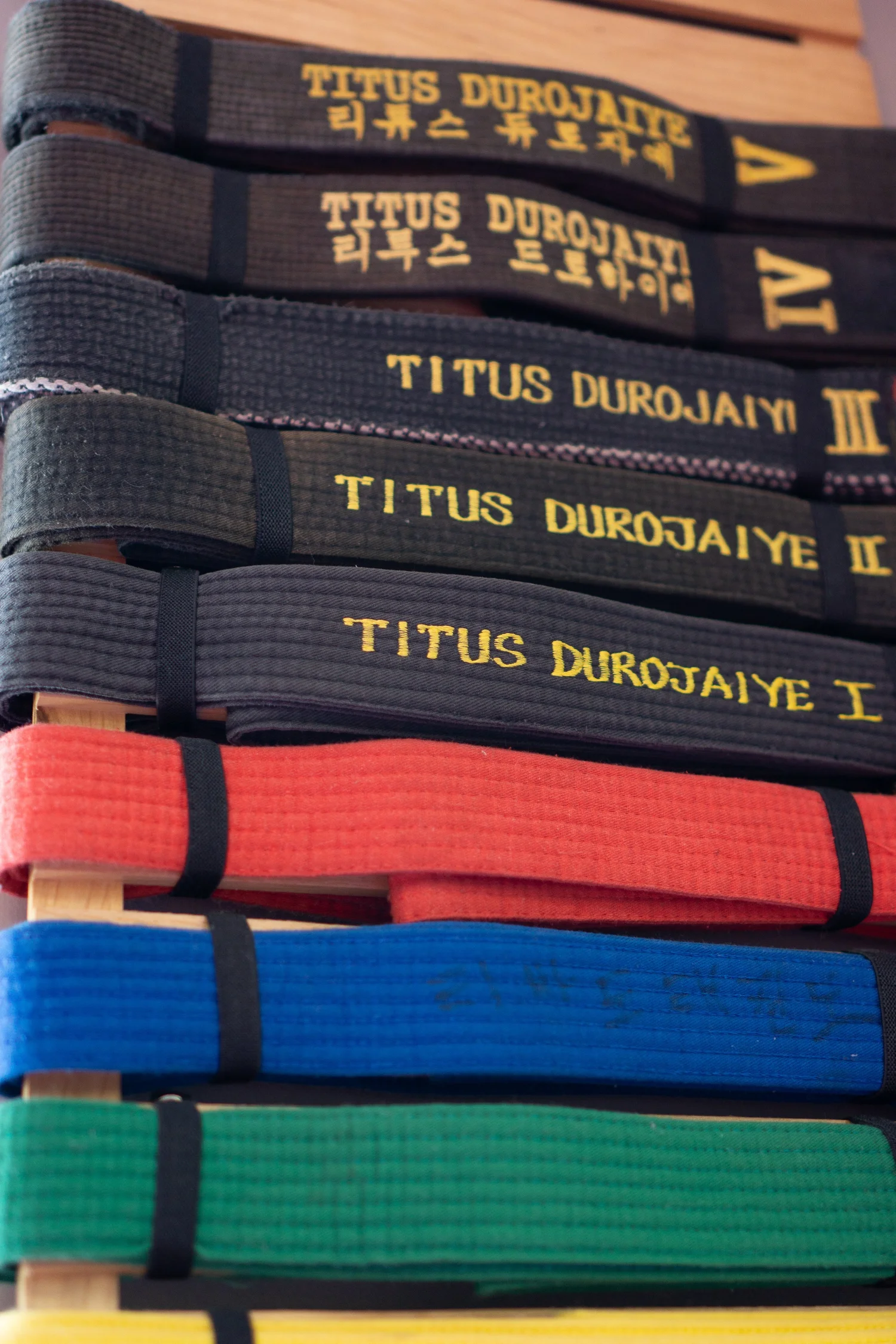 A stack of black belts embroidered with Titus Durojaiye's name marking each dan rank