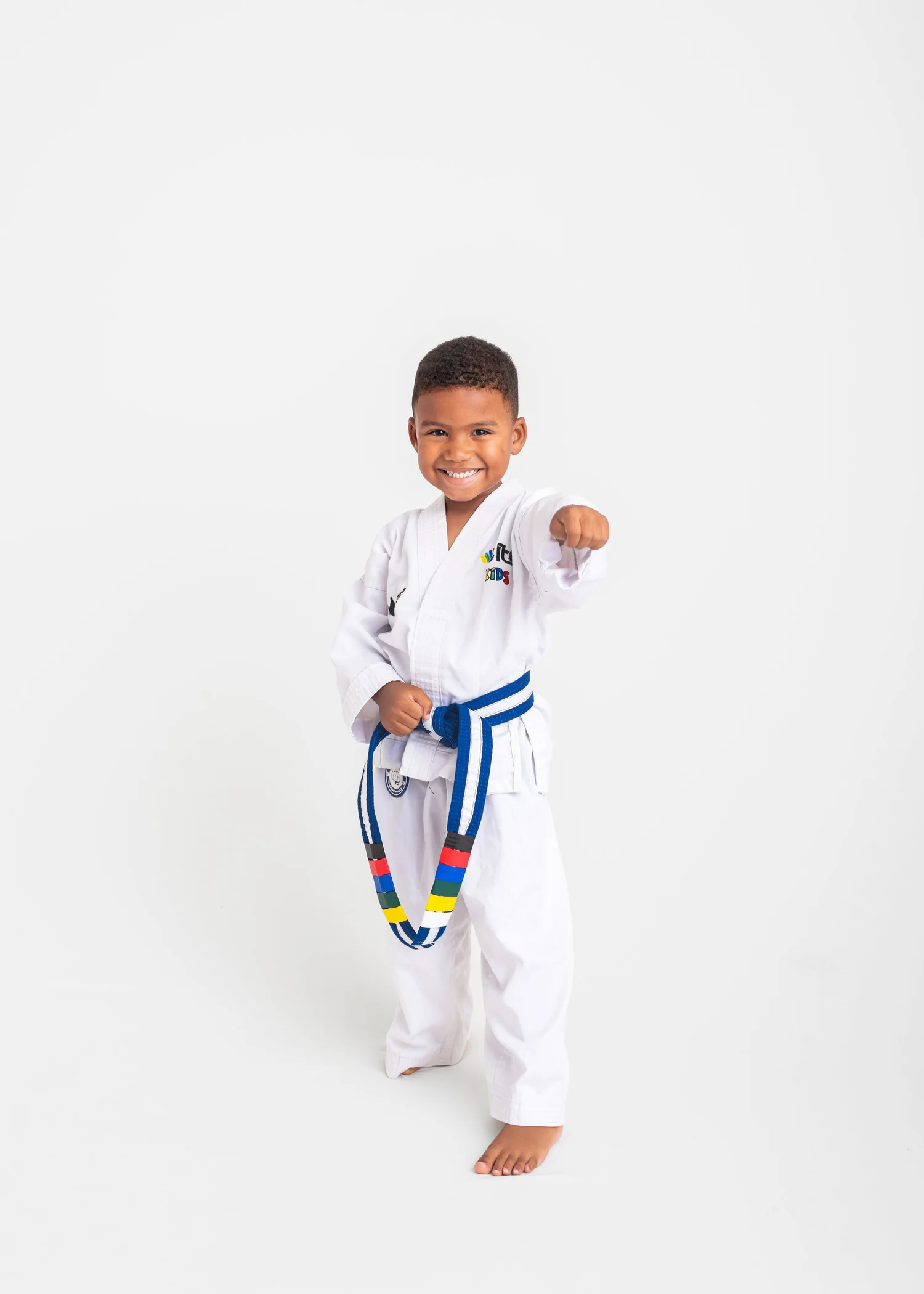 A young Mini Taekwon-Do student in a white uniform and blue belt, fist raised