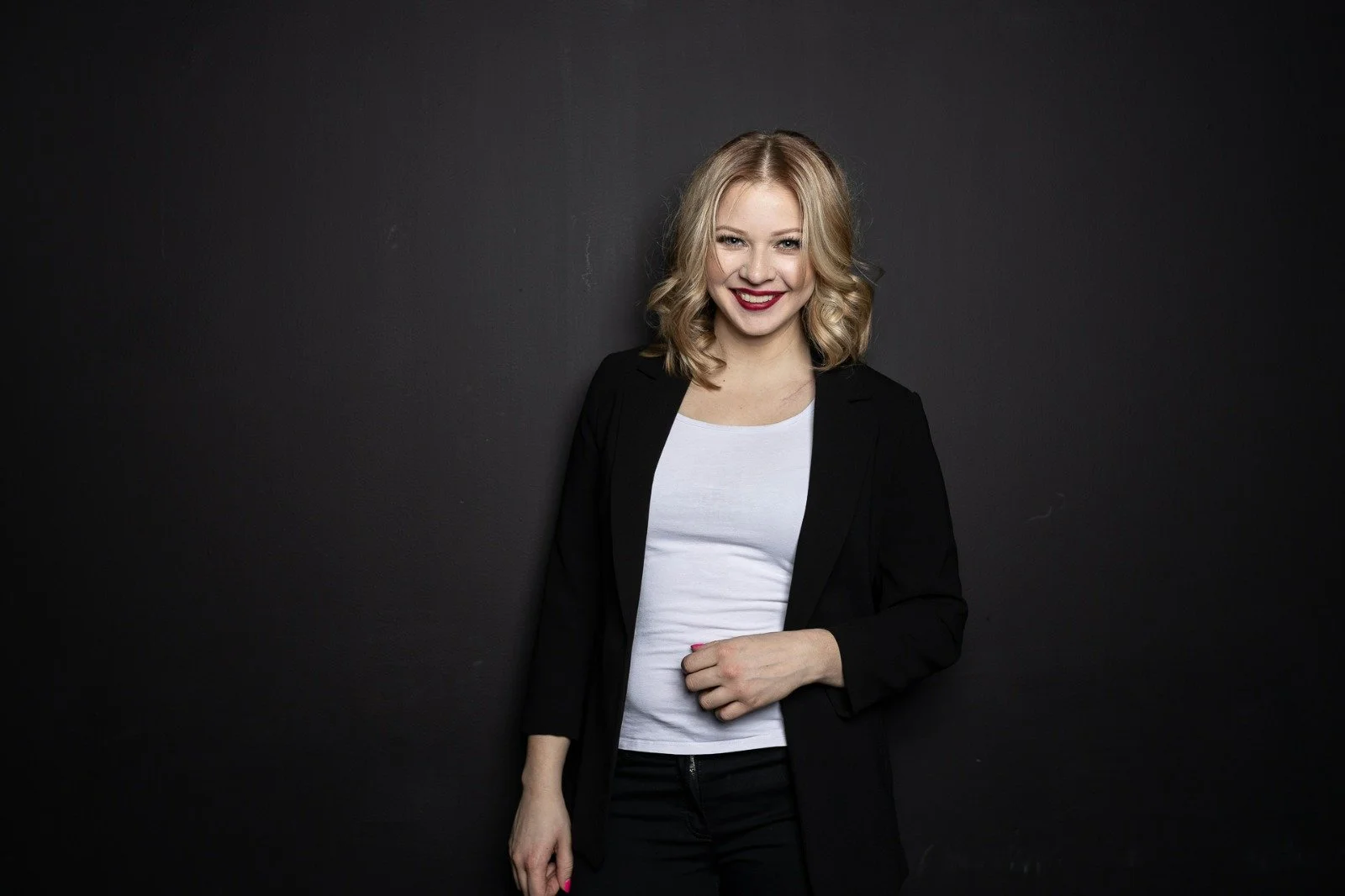 Smiling person in a blazer and white shirt standing against a black background.