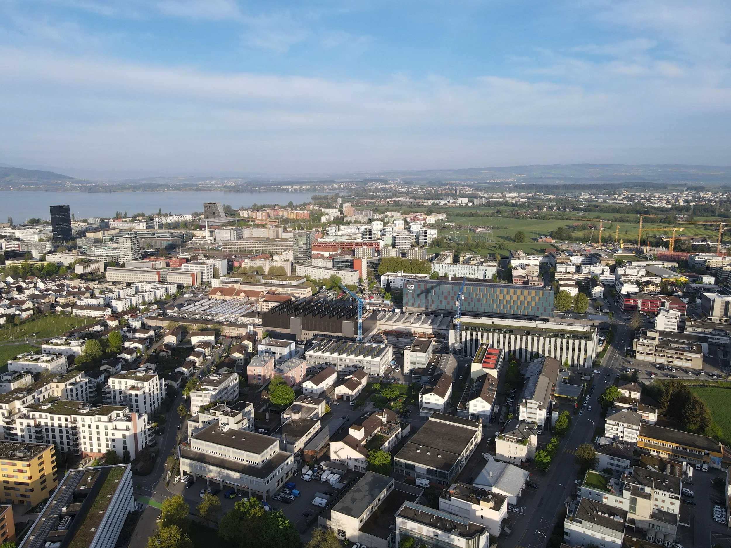 Luftaufnahme einer Stadt mit angrenzendem Fluss und grünen Feldern im Hintergrund.