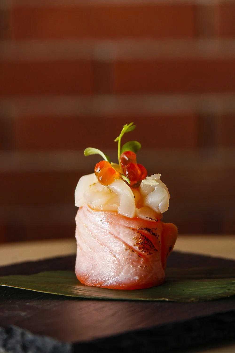 Gourmet prato com fatia de peixe, coberto com cream cheese, pimenta em conserva, cebola e microverdes, apresentado sobre uma folha de bananeira