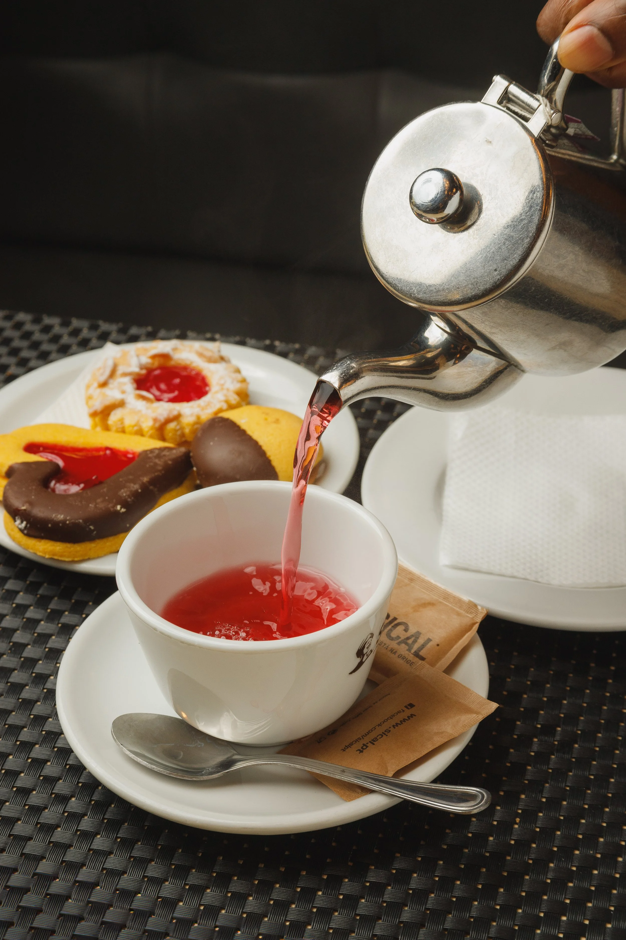 Chá vermelho sendo servido em uma xícara branca, com alguns cookies e biscoitos decorados ao fundo.