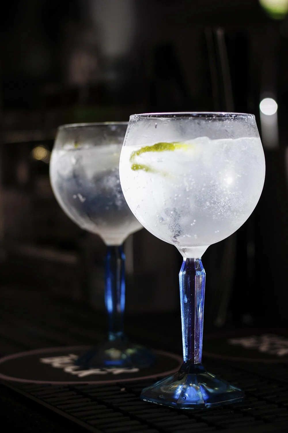 Dois copos de coquetel com gelo e limão, com um fundo escuro.