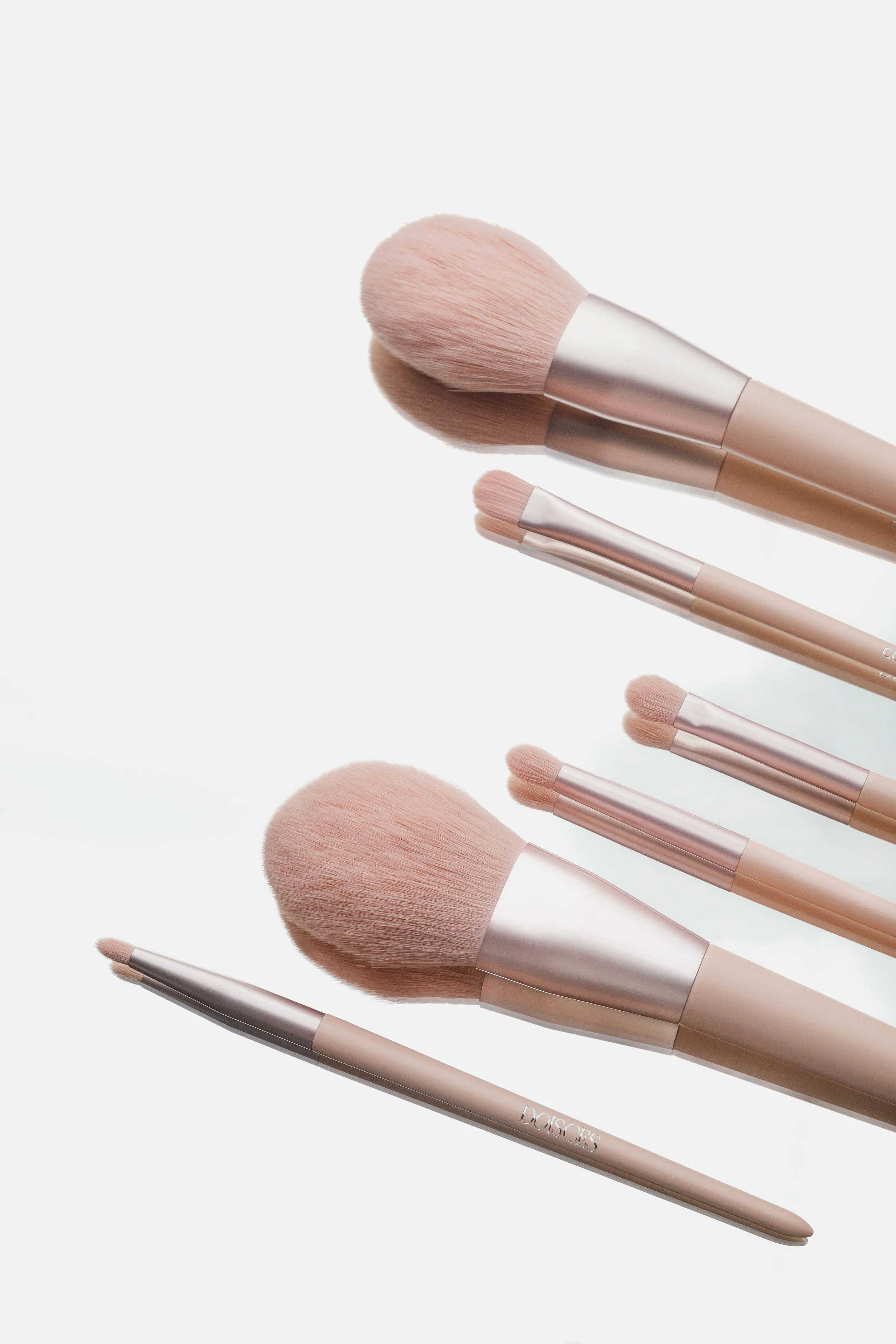 Conjunto de pincéis de maquiagem com cabos em tom rosé, variados tamanhos e formatos, dispostos sobre fundo branco.