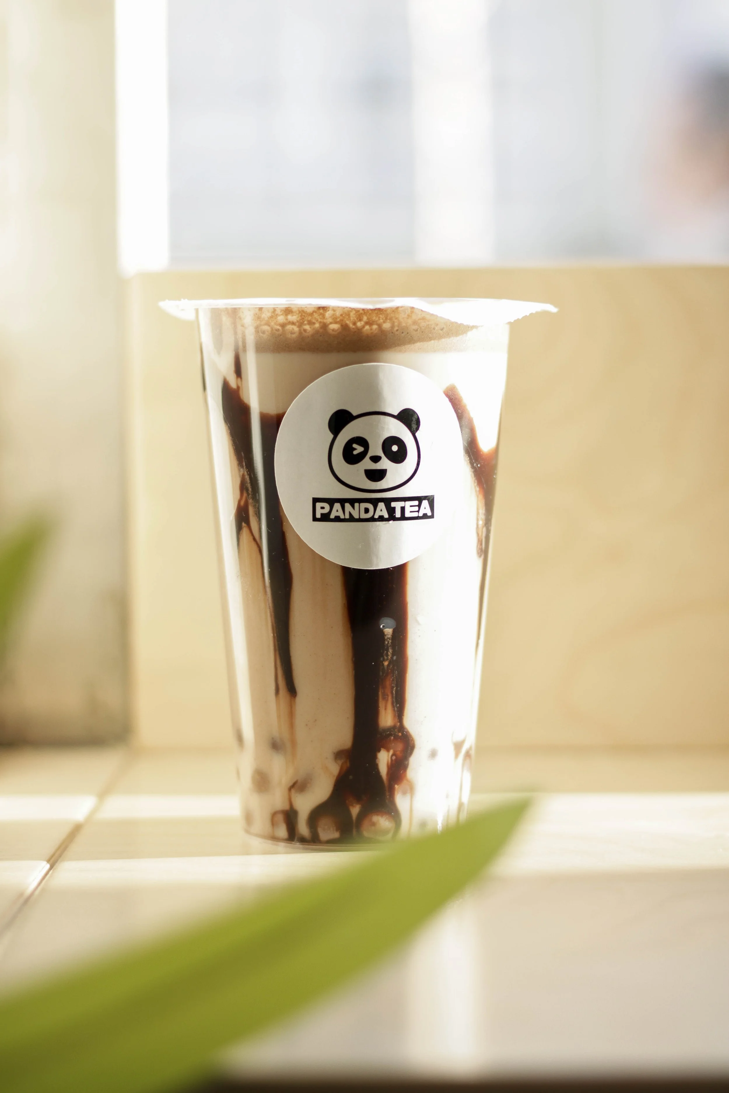 Copo de chá de bolhas com pronome de marca Panda Tea, com logo de panda lobo e o nome Panda Tea, com gotas e raspas de chocolate