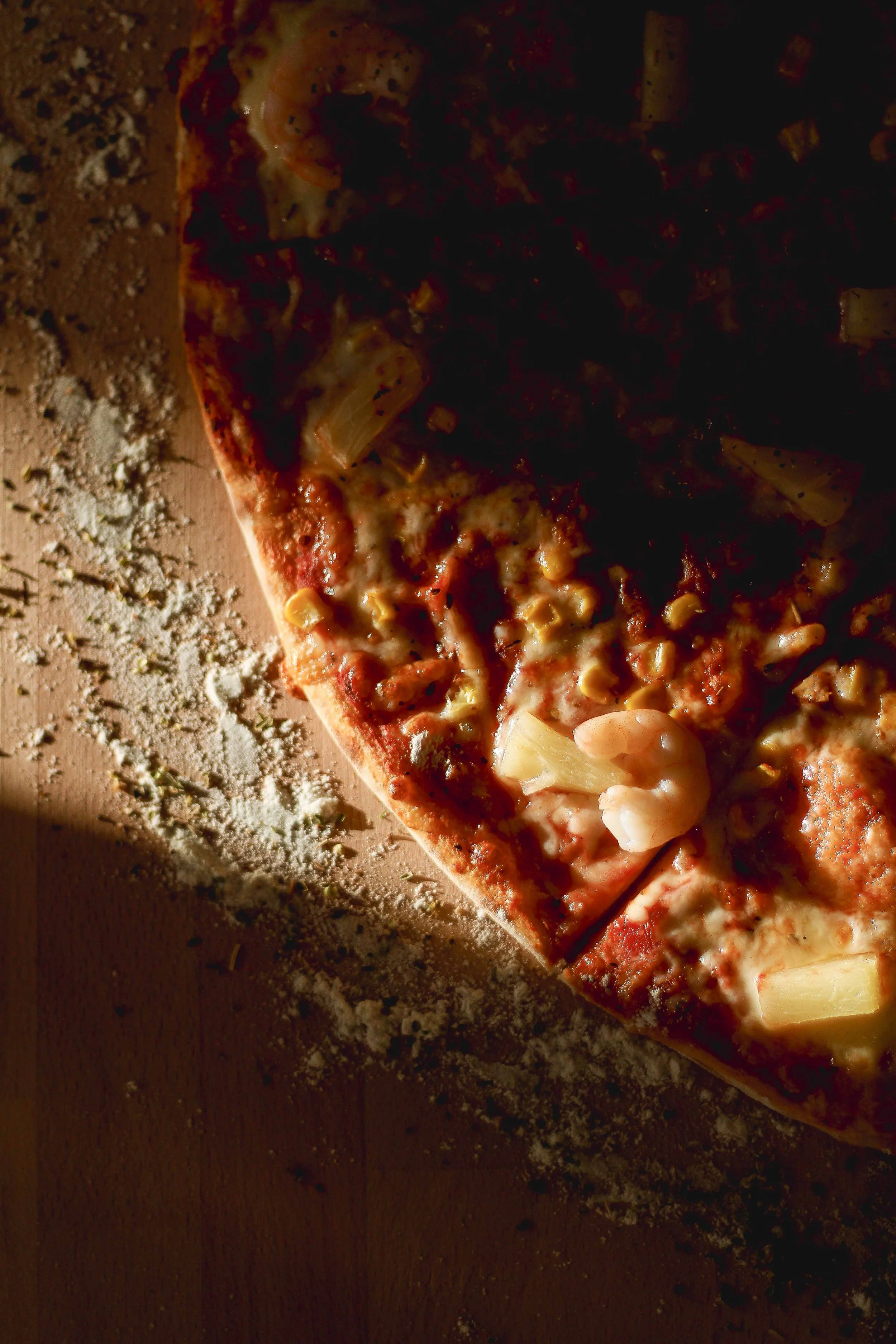 Fatia de pizza com queijo, pedaços de frango e cebola, sobre uma mesa de madeira com farinha espalhada ao redor.