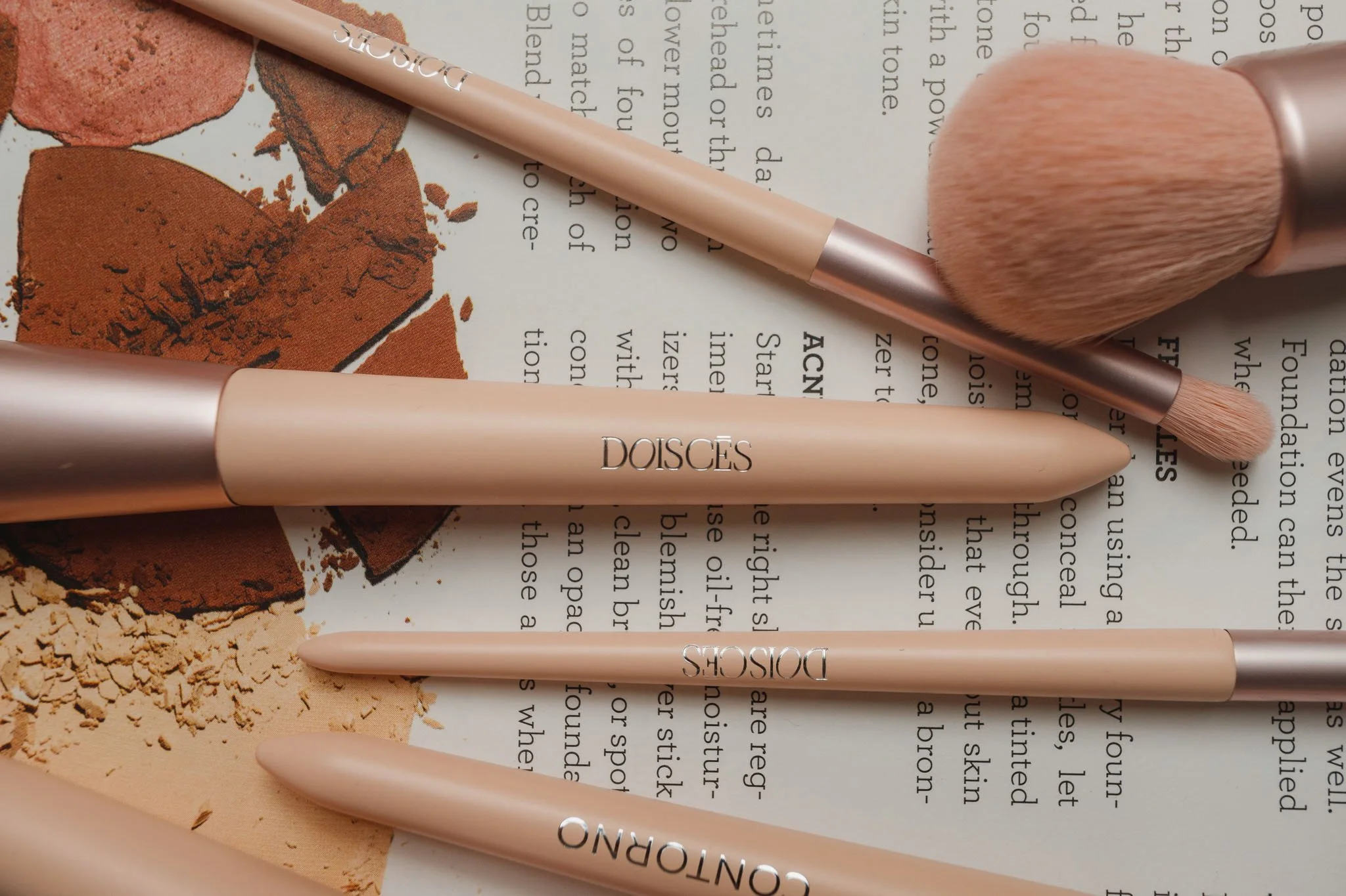 Conjunto de pincéis de maquiagem sobre uma página de livro ou revista, com pó de maquiagem e sombra de olhos.