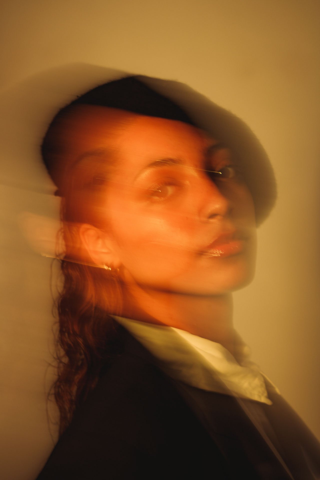 Retrato artístico de uma mulher com cabelo cacheado, usando jaqueta e maquiagem, com efeito de movimento e desfoque, luz quente