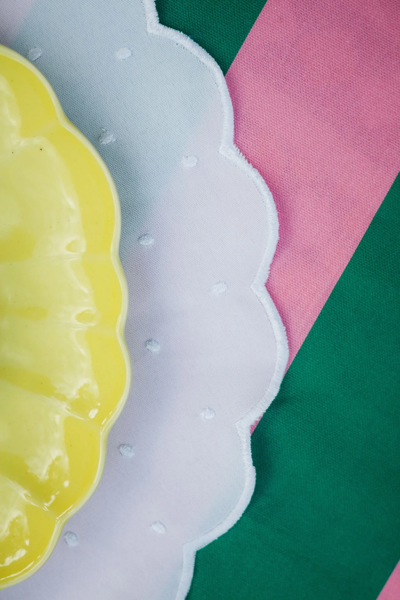 Detalhes de uma toalha com cores verde, rosa, branca e uma peça de material amarelo com relevo na superfície