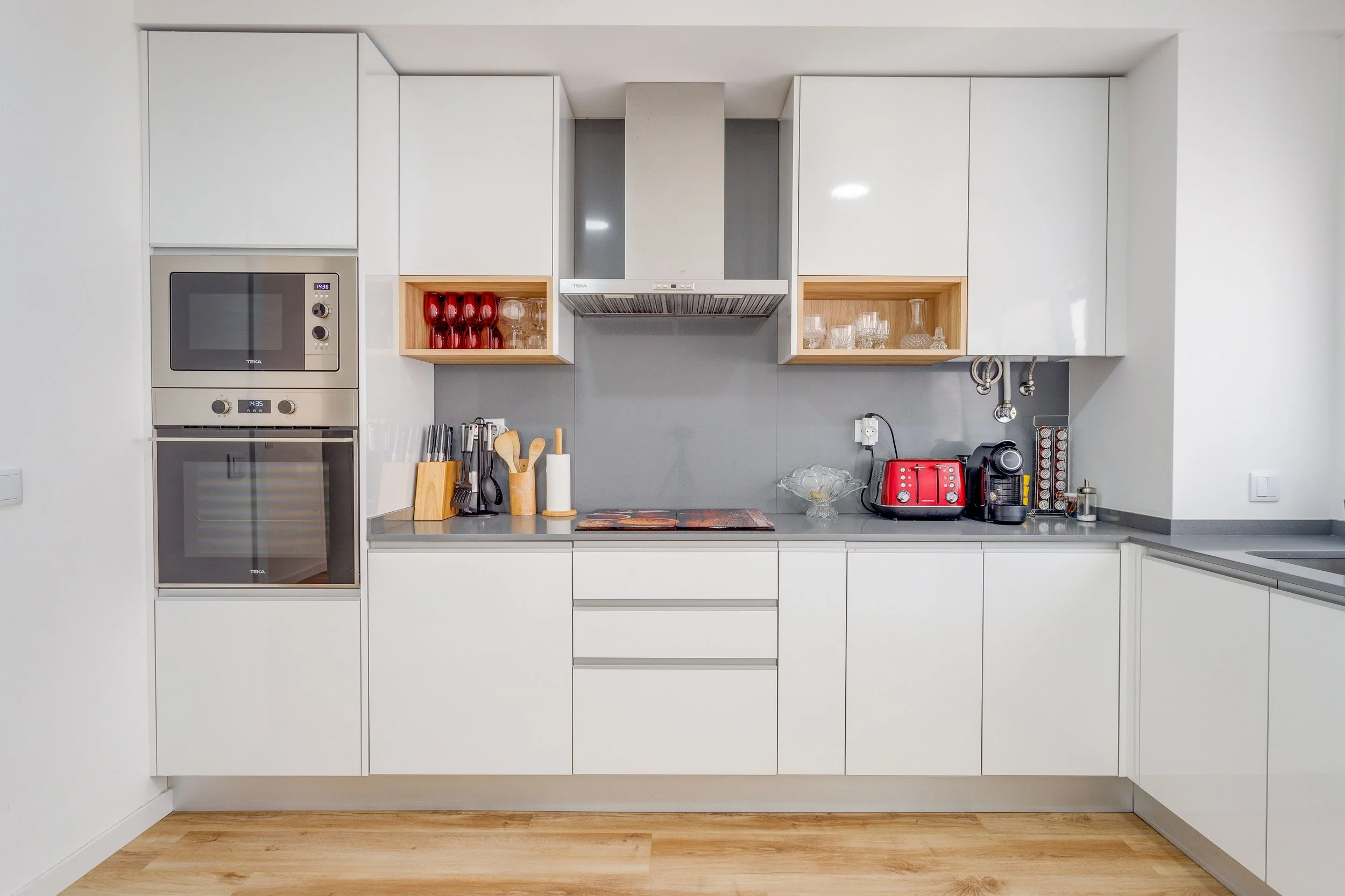 Cozinha moderna com armários brancos, geladeira, forno, micro-ondas, utensílios de cozinha, tostadeira vermelha e máquina de café.