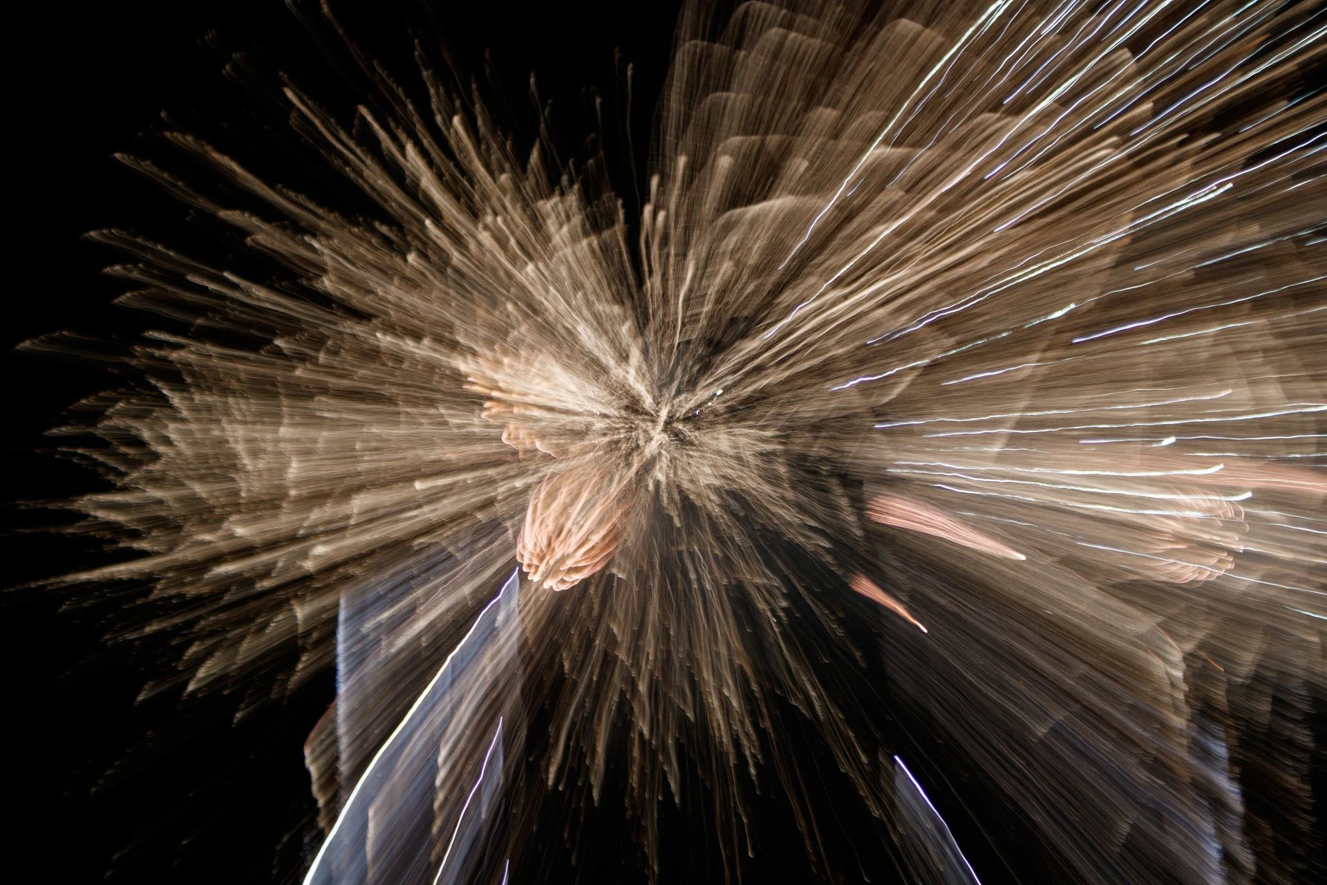 Fogos de artifício explodindo no céu escuro, com rajadas de luz dourada e branco.