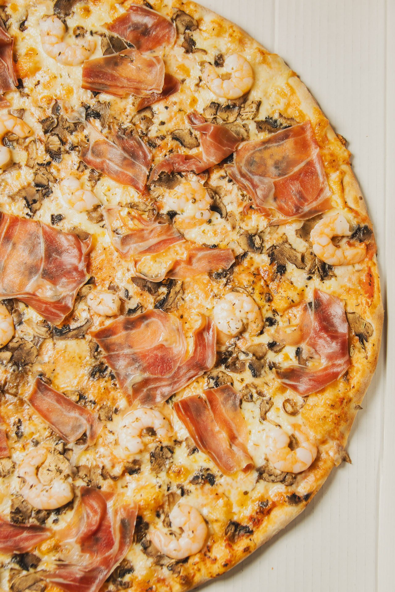 Pizza de tamanho grande com cobertura de presunto, camarão, queijo e cogumelos.