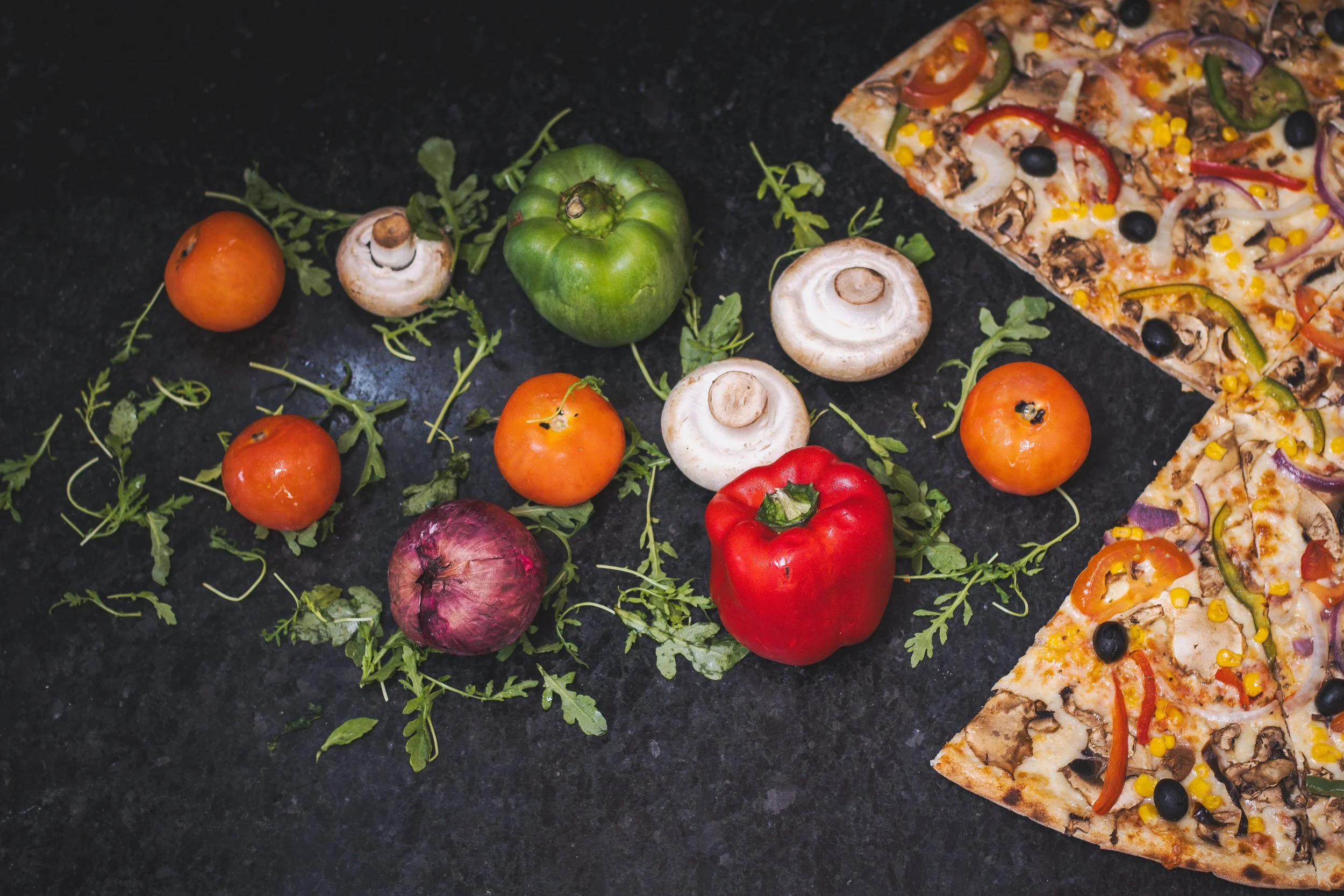 Casca de tomate, cogumelo, pimentão vermelho, cebola roxa e tomate cereja ao lado de fatias de pizza de legumes.