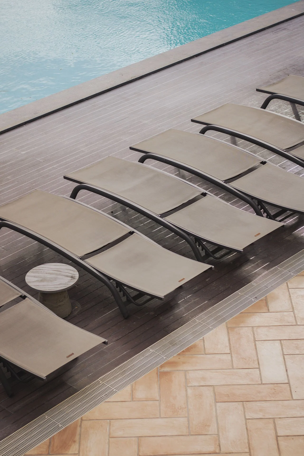 Cadeira de piscina vazia ao lado de uma piscina, com piso de madeira escura ao lado de piso de cerâmica clara.