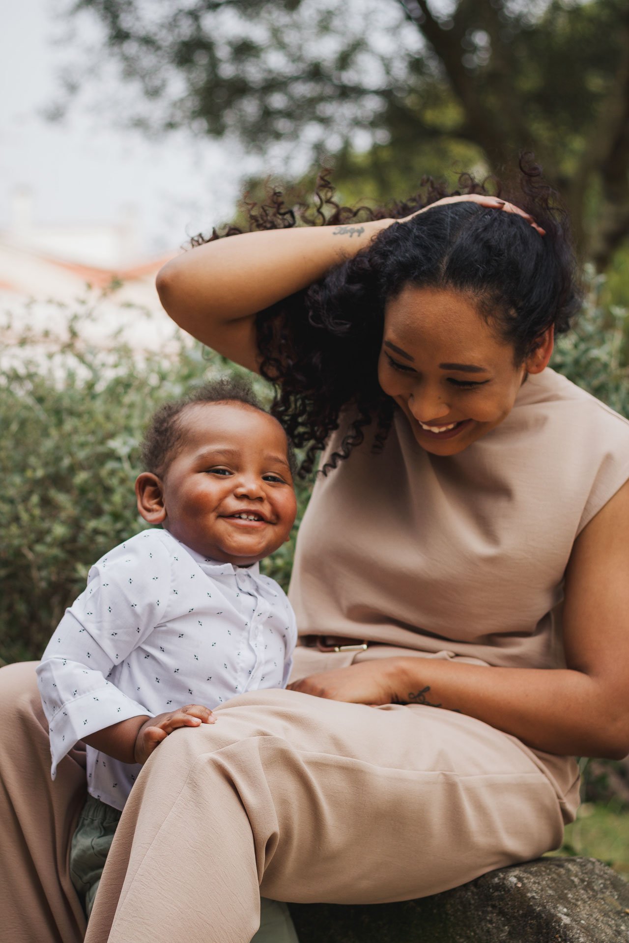 Mulher e criança sorrindo ao ar livre, com árvores ao fundo.