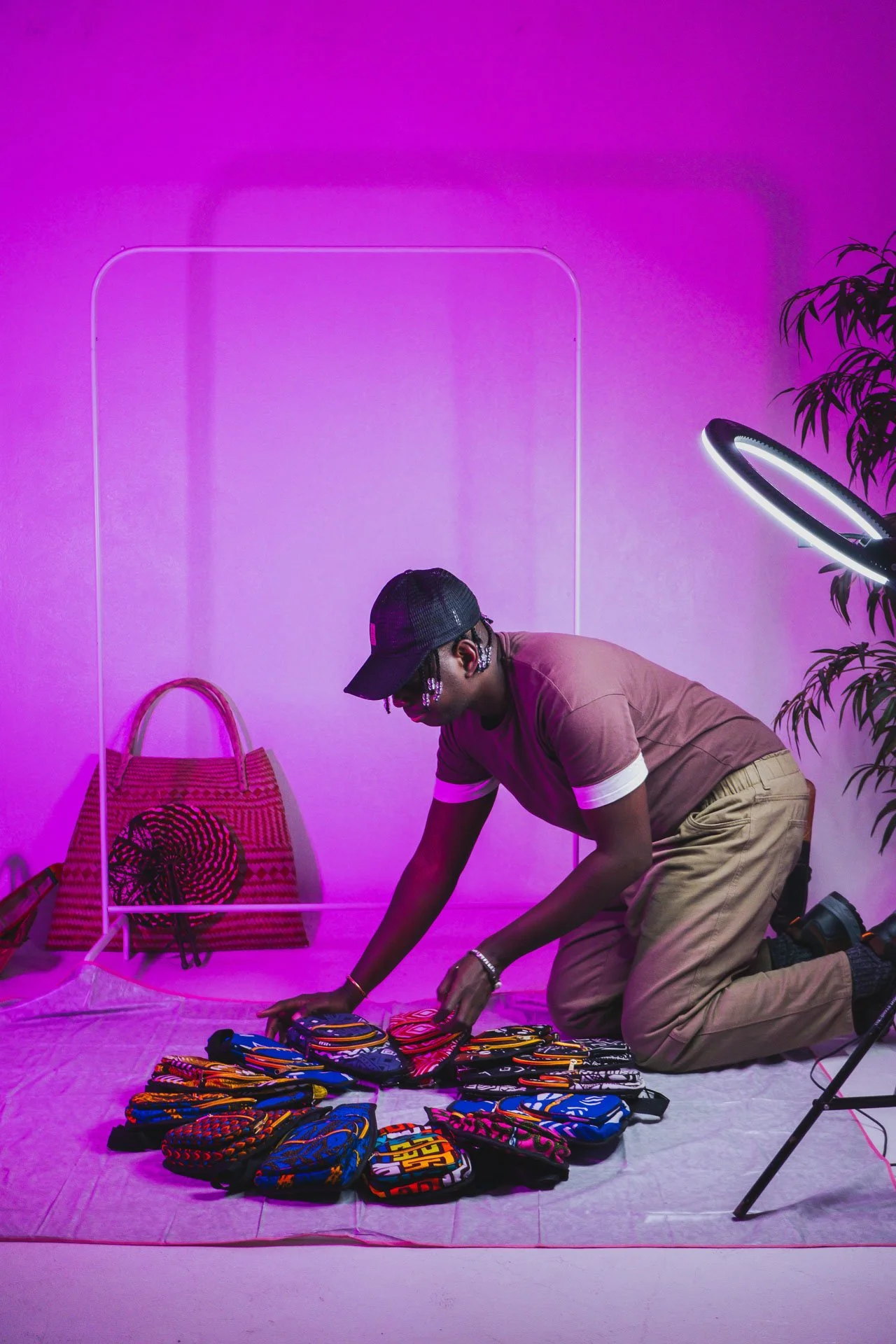 Homem de joelhos organizando small bolsas de tecidos coloridos em um fundo roxo com iluminação de ring light do lado direito.