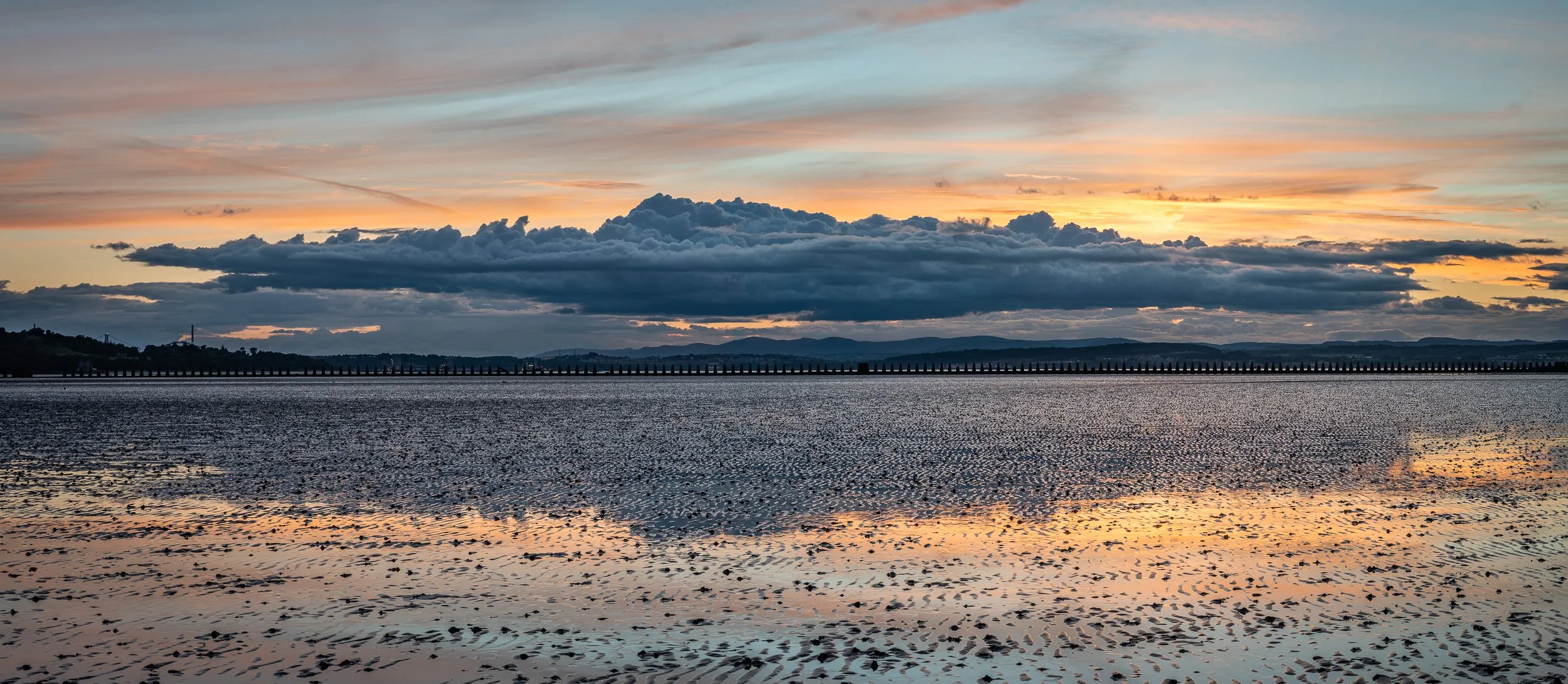 Sunset over a body of water with clouds and mountain silhouette in the background.