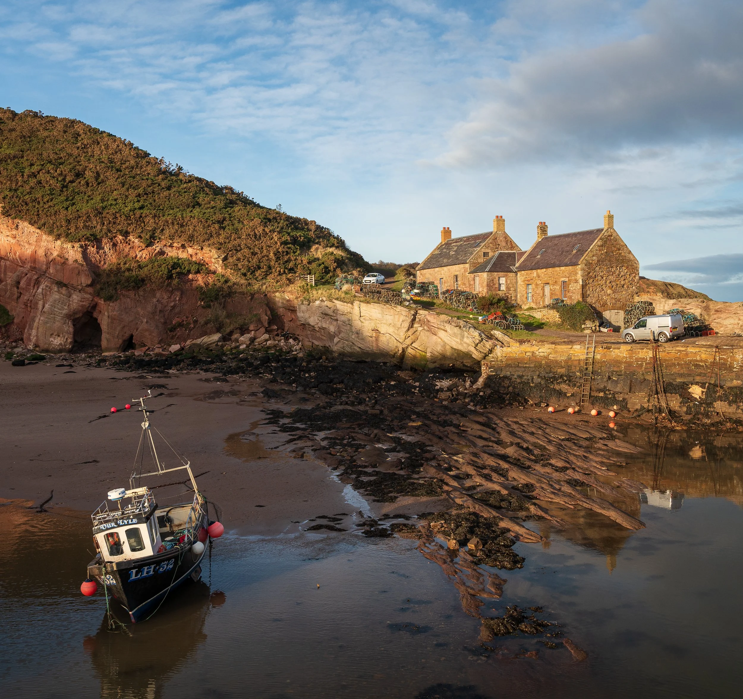 A small boat anchored near the shore with a house and hills in the background, captured during sunset.