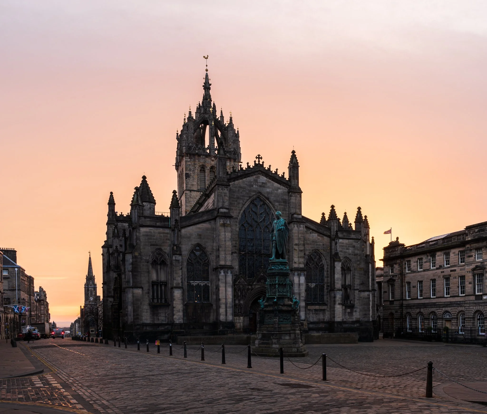 A historic church with gothic architecture at sunset, surrounded by cobblestone streets and historic buildings.