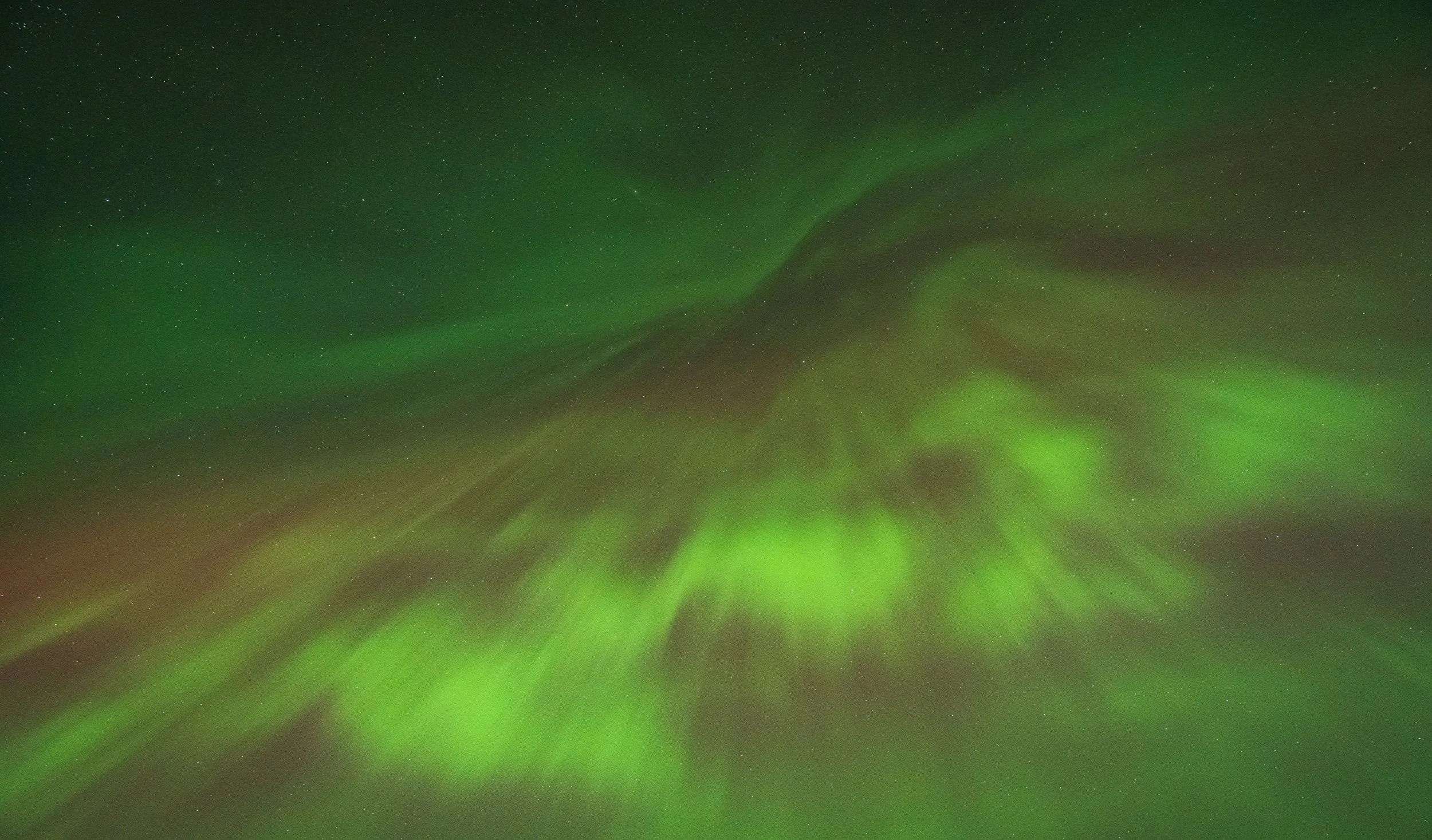 Northern lights with green hues illuminating the night sky filled with stars.