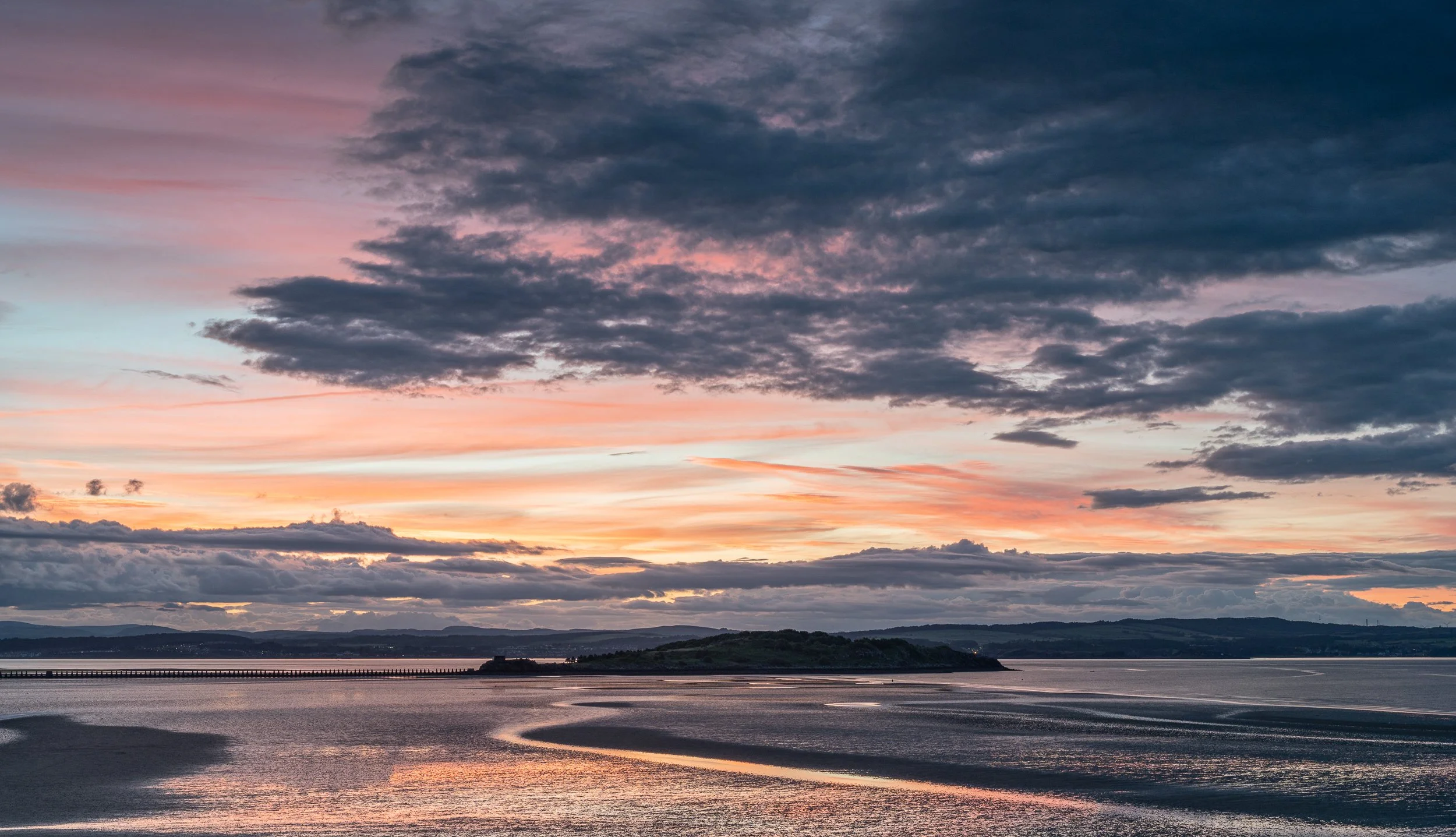 A tranquil sunset over a body of water with colorful clouds in the sky and a distant hill.