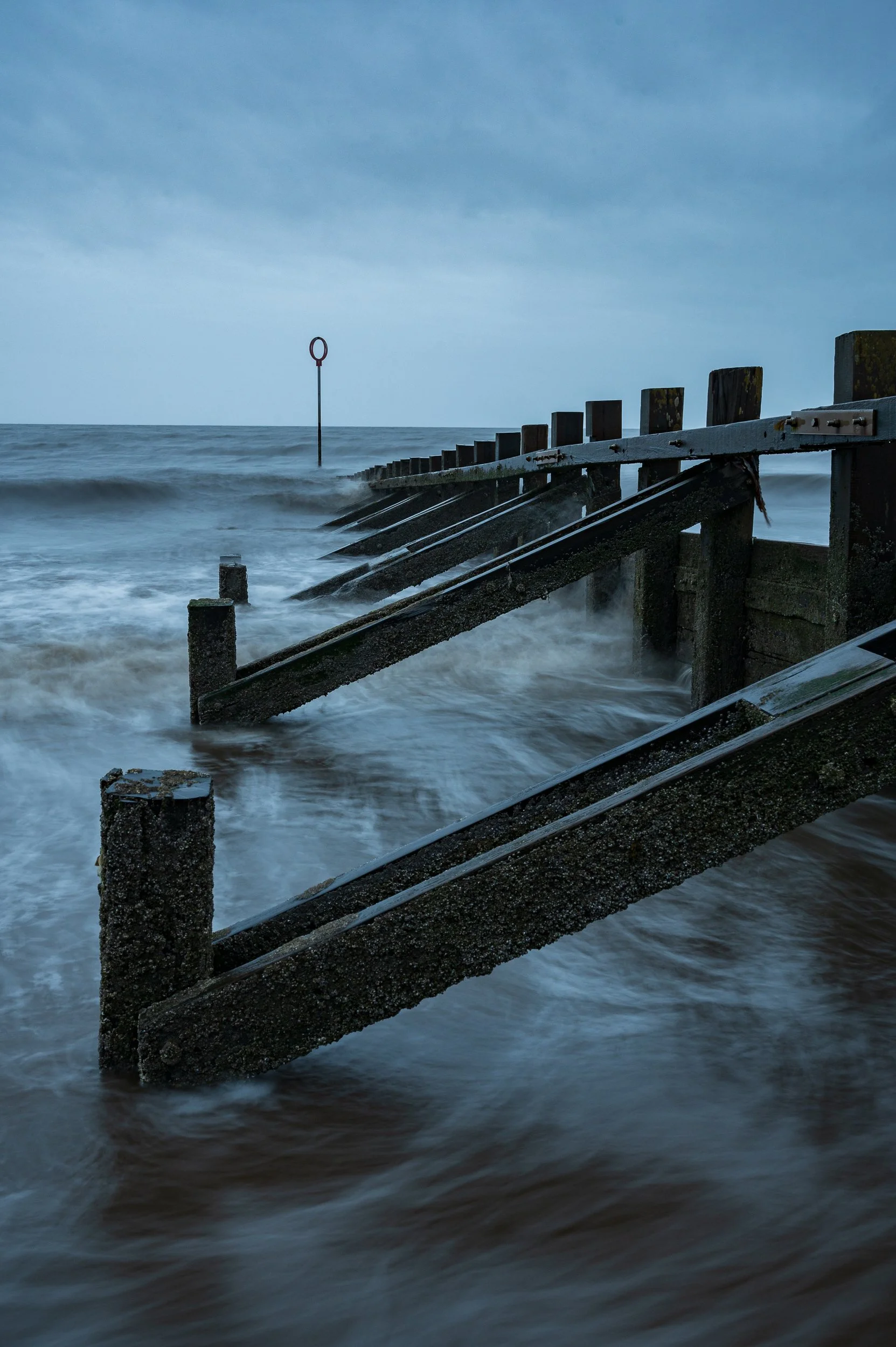 Stormy sea with broken wooden pier and a navigational marker in the background.