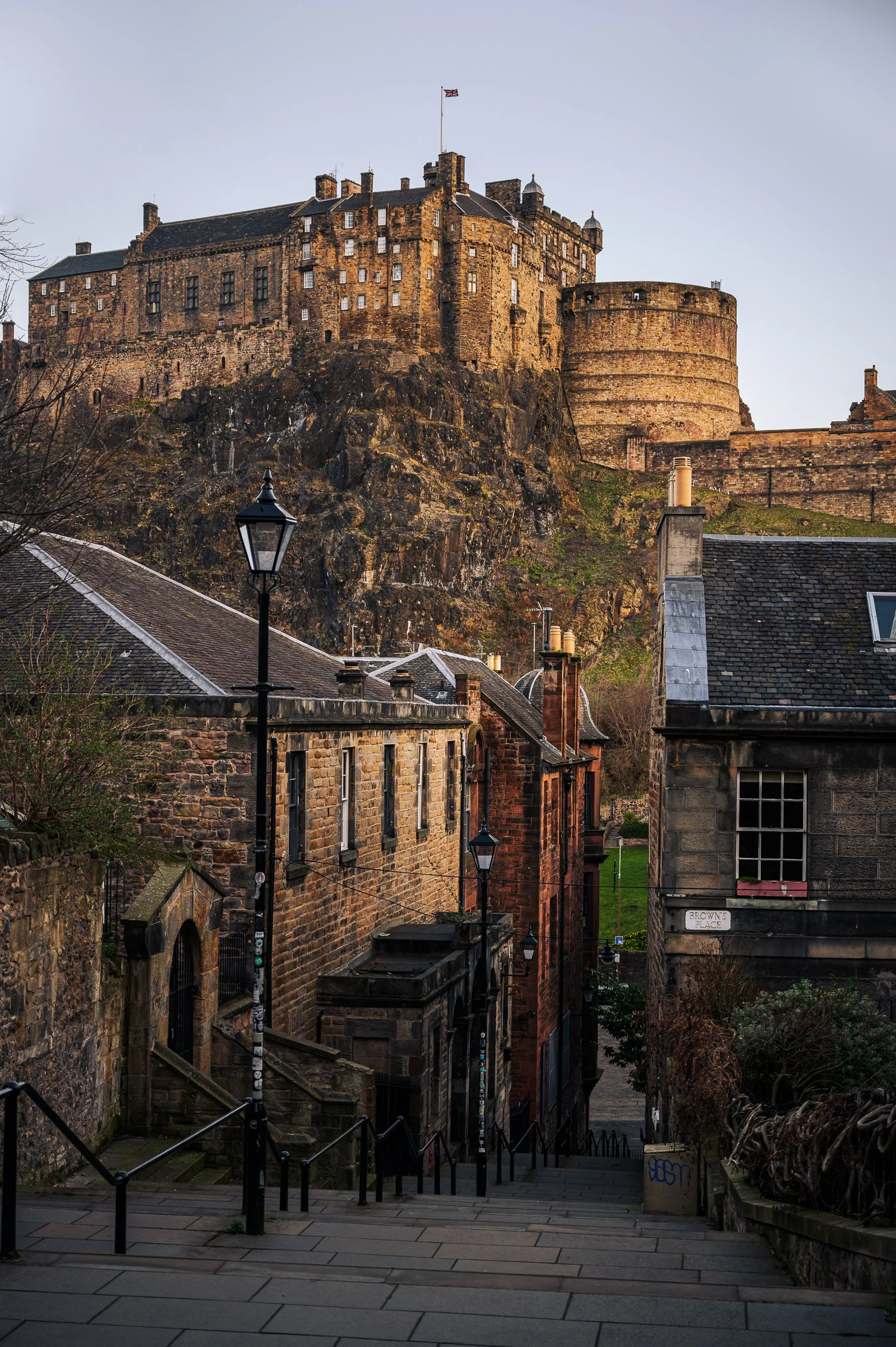 View of Edinburgh Castle on a hill overlooking old stone buildings and a street with lampposts.