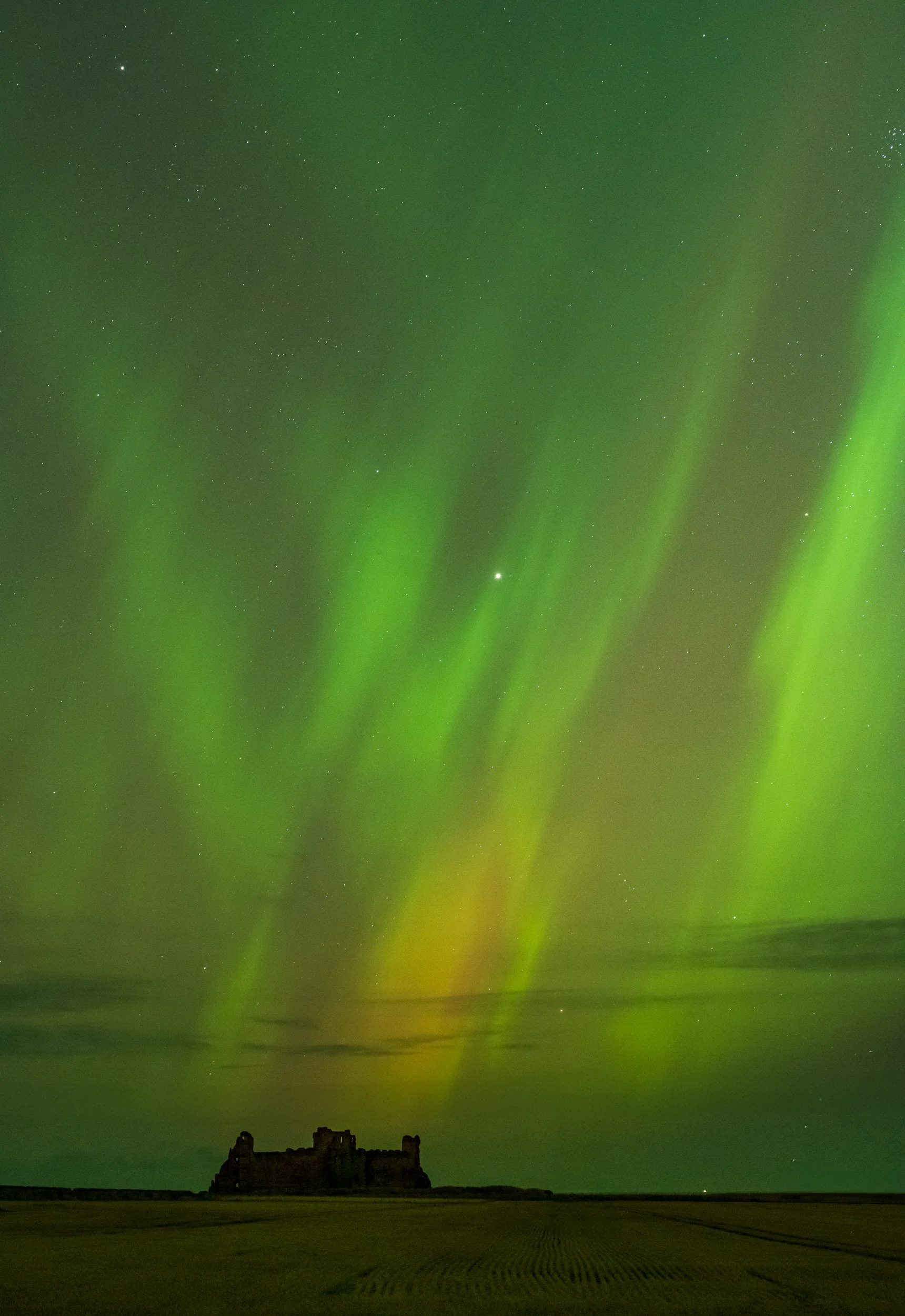 Northern lights over a dark landscape with a silhouette of an old castle or fort.