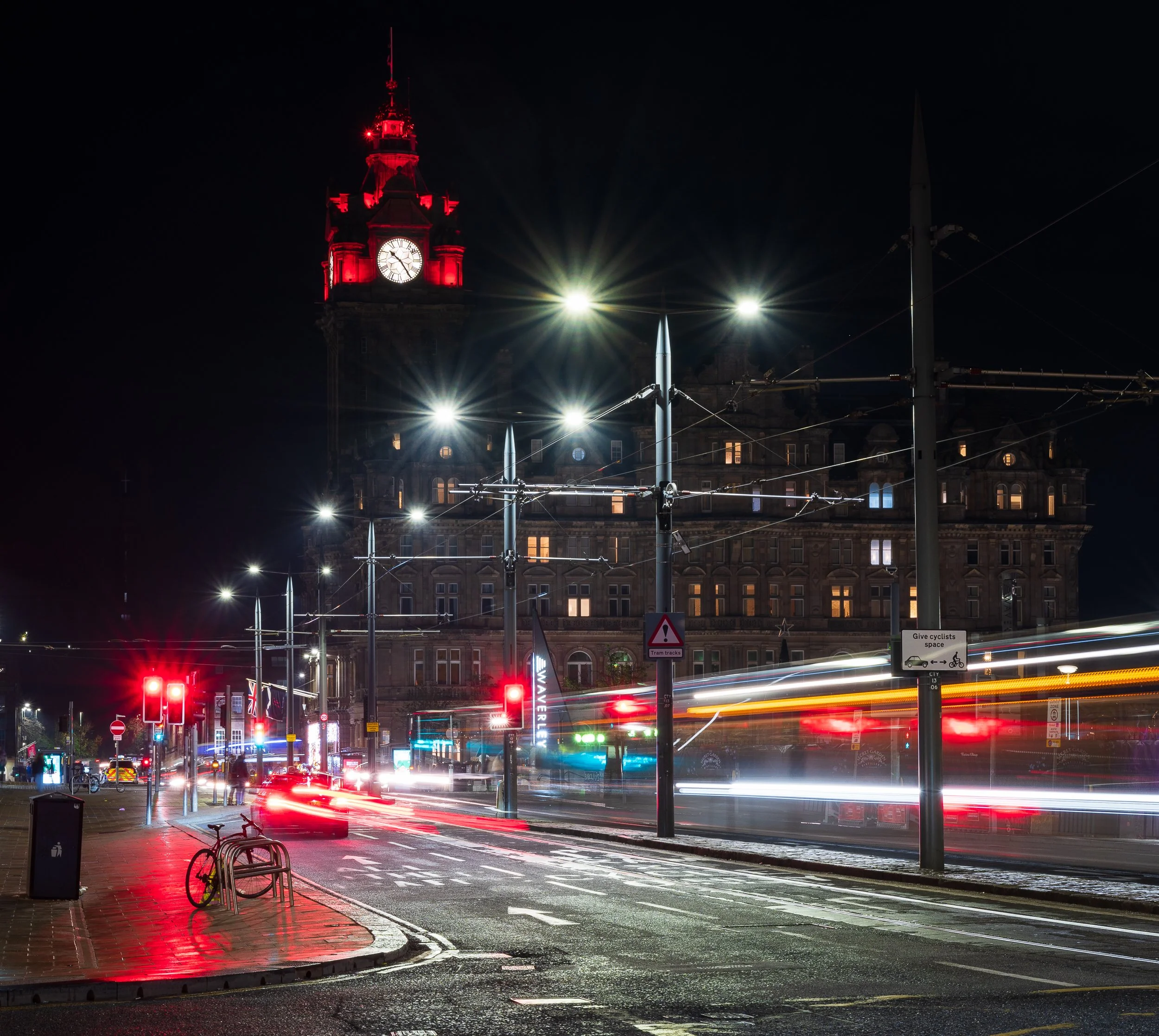Nighttime city street scene with the clock tower lit in red and light trails from moving vehicles.