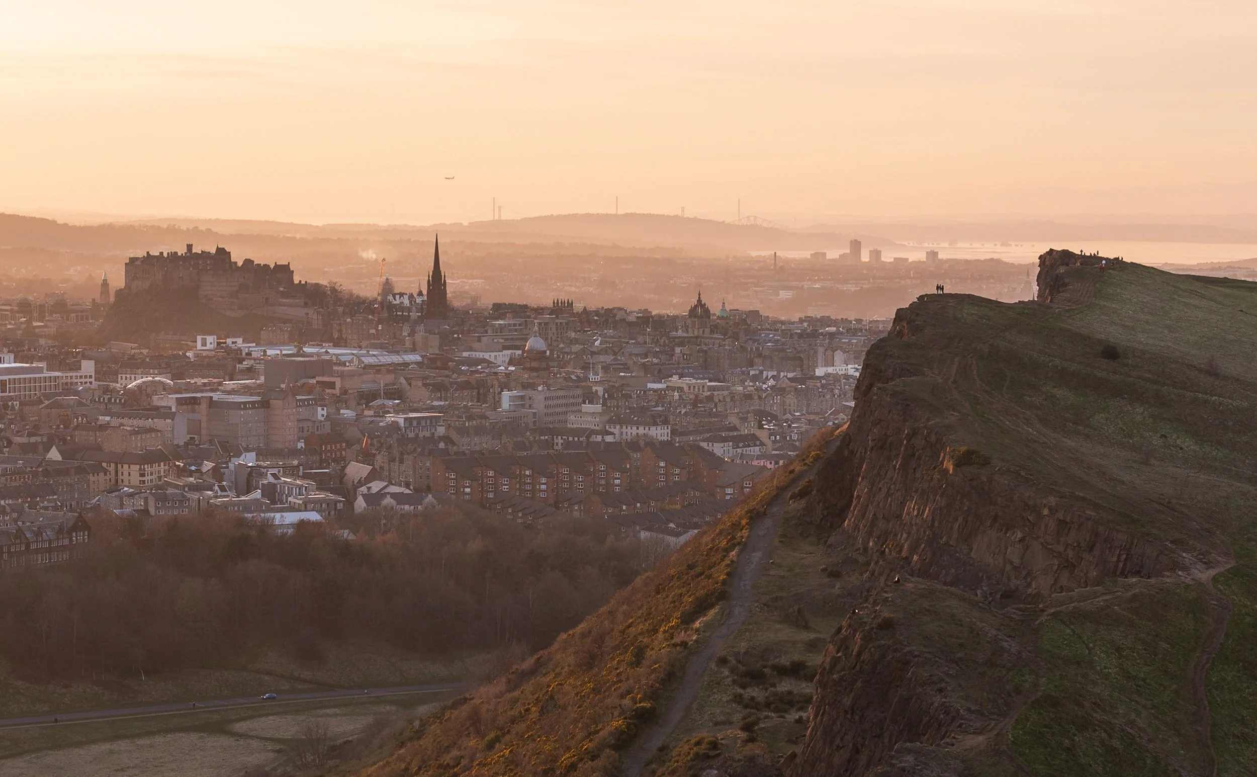 Sunset over Edinburgh cityscape featuring Edinburgh Castle and Salisbury Crags.