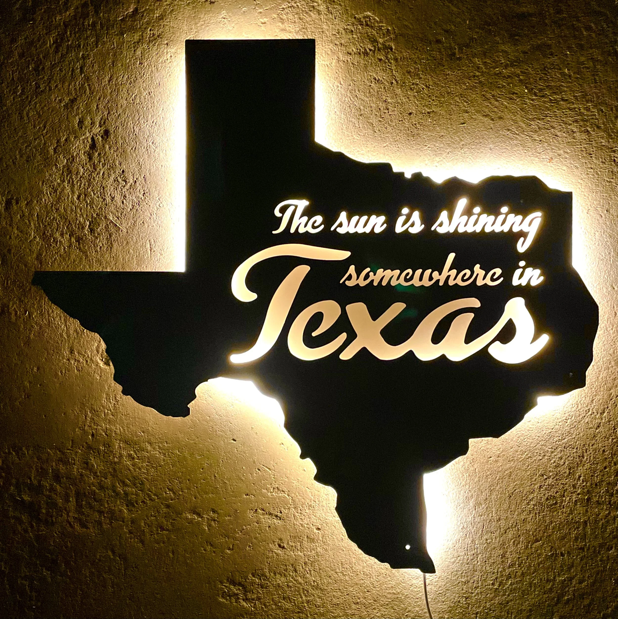 Backlit metal sign wall decoration of the state of Texas with the phrase 'The sun is shining somewhere in Texas' written on it.