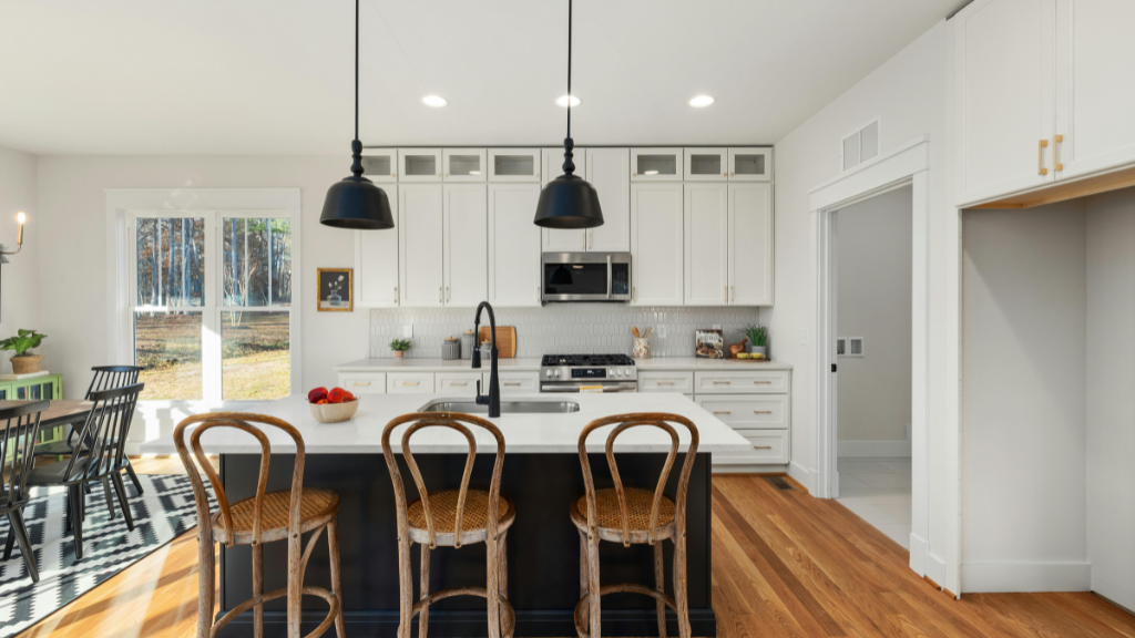 Modern kitchen with white cabinets, stainless steel refrigerator, microwave, and black and white patterned backsplash. Central island with a sink and decorative items, including a planter and tray.