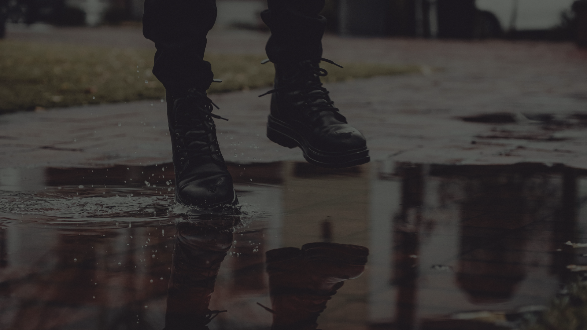 Person wearing black boots walking through a puddle on a wet outdoor surface.