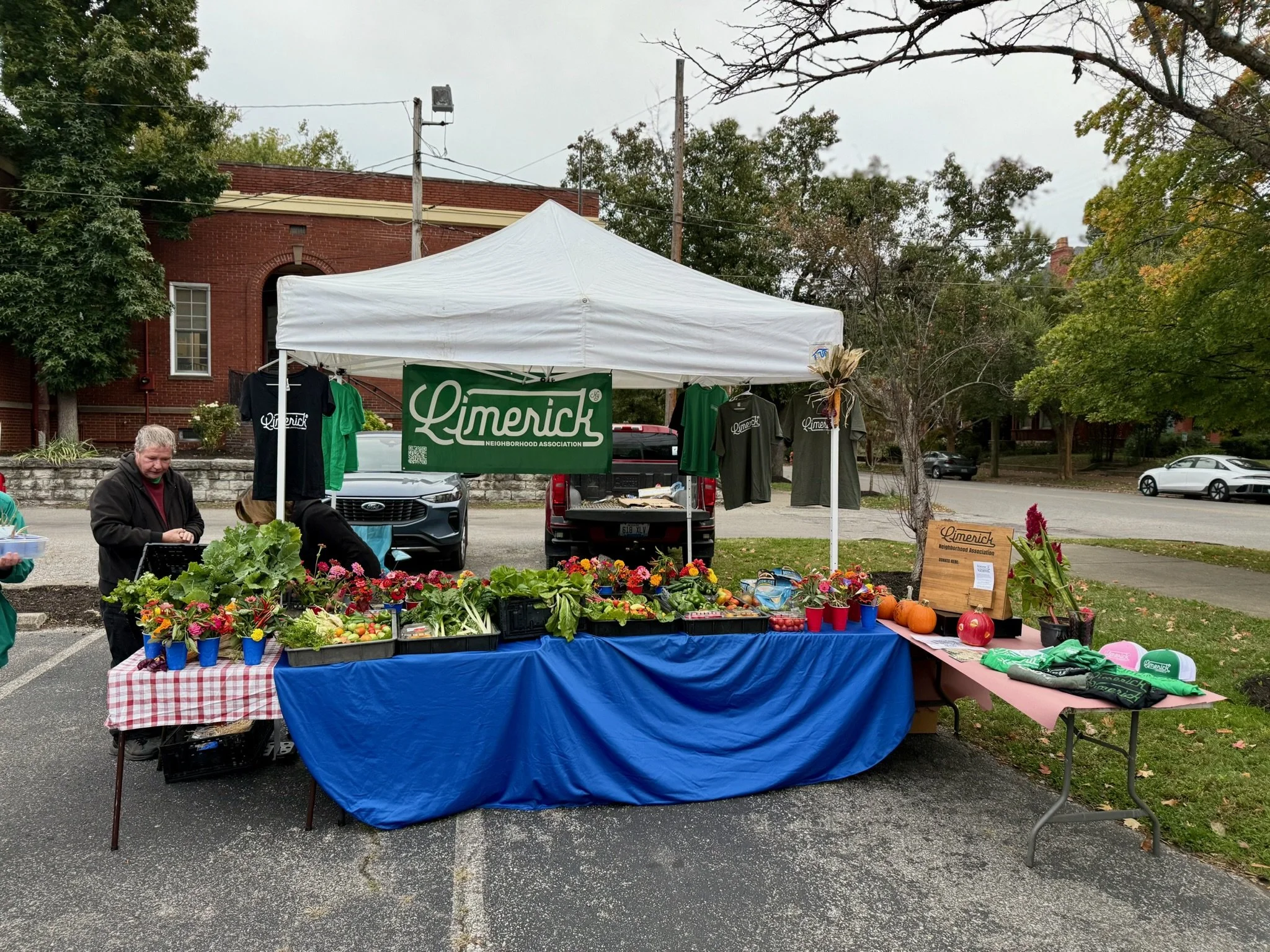 Limerick Neighborhood Association market stall displaying flowers, vegetables, and Limerick T-shirts.