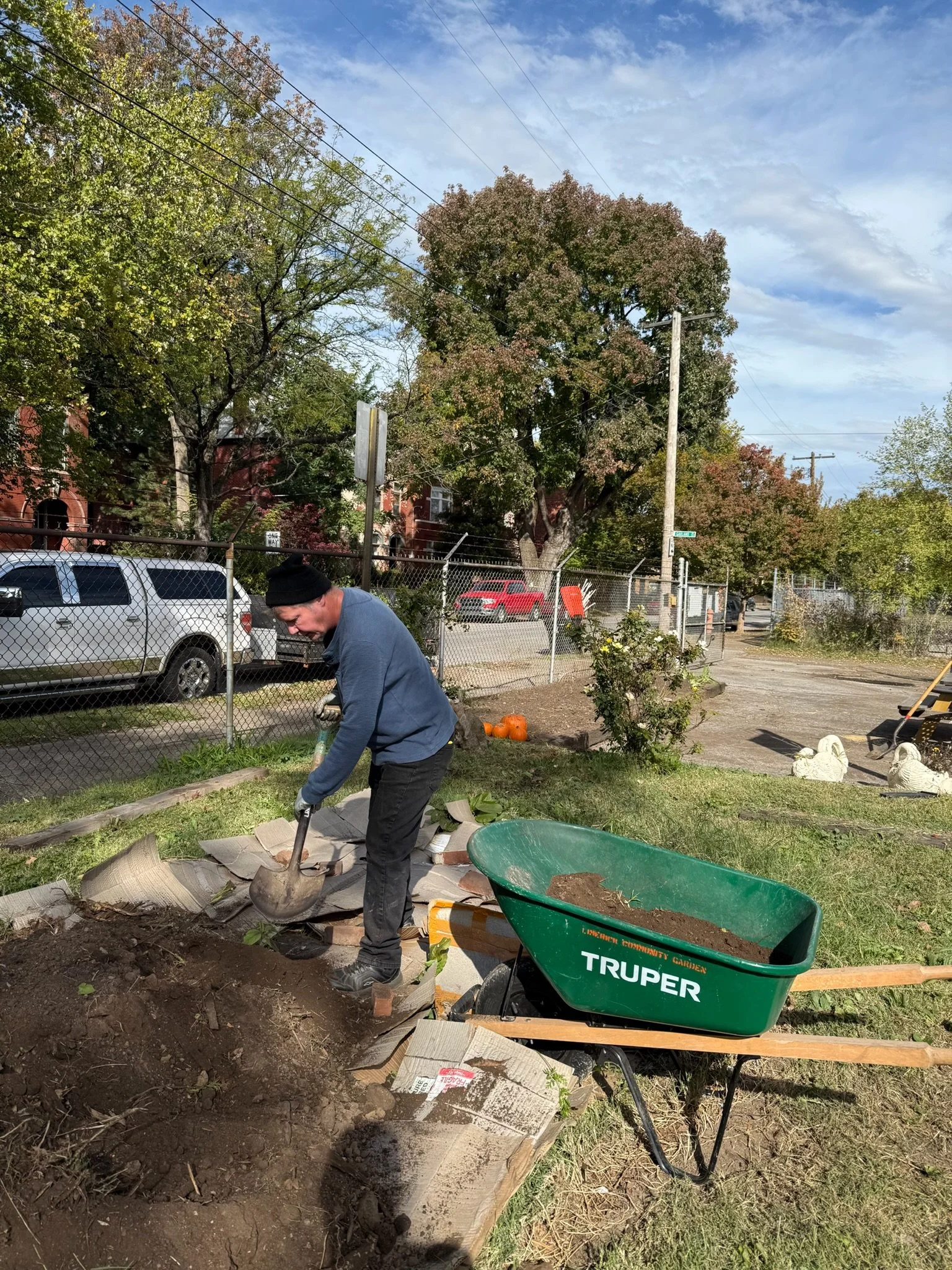 Limerick Community Garden volunteer digging in a garden bed with a green wheelbarrow nearby.