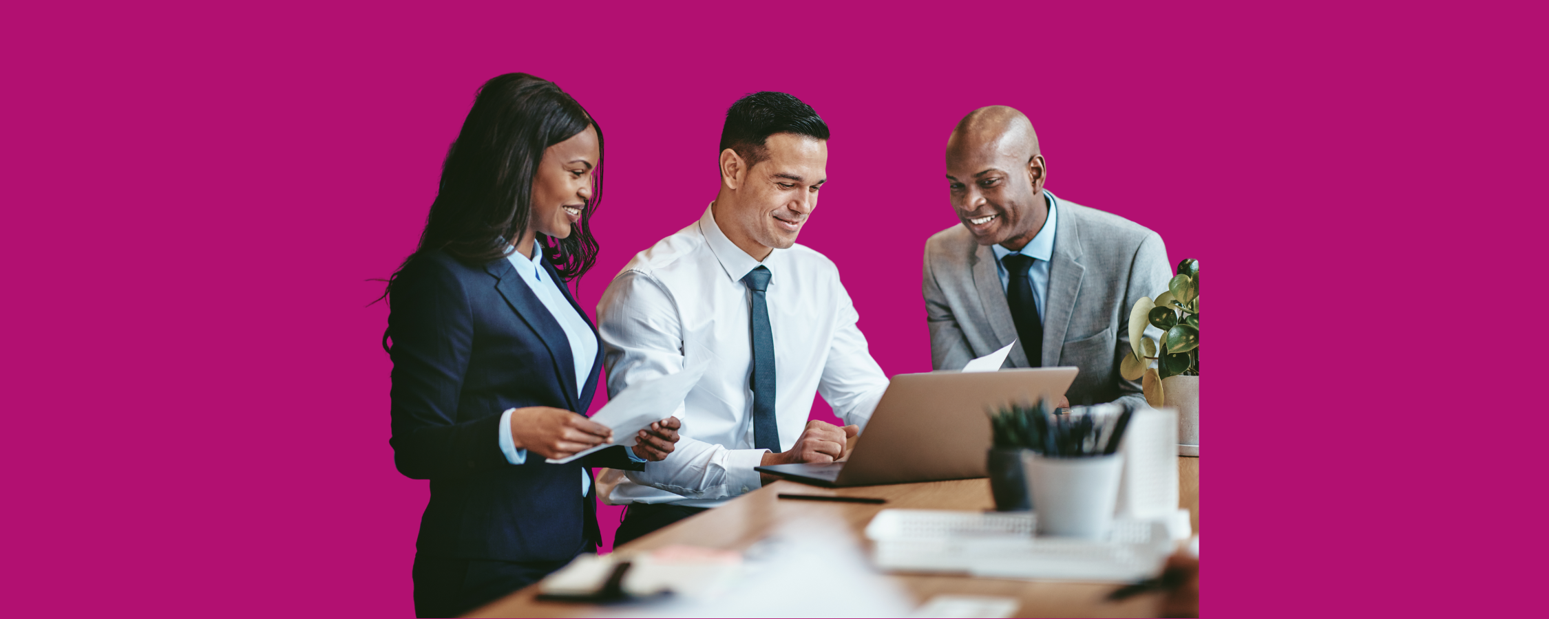 Three professionally dressed colleagues smiling and collaborating at a laptop in a bright, modern office setting, with a bold magenta background.