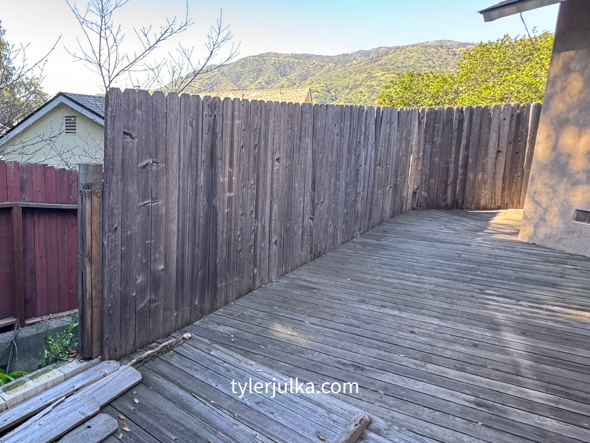 Wooden backyard deck with fencing, trees, and mountains in the background, in sunlight.