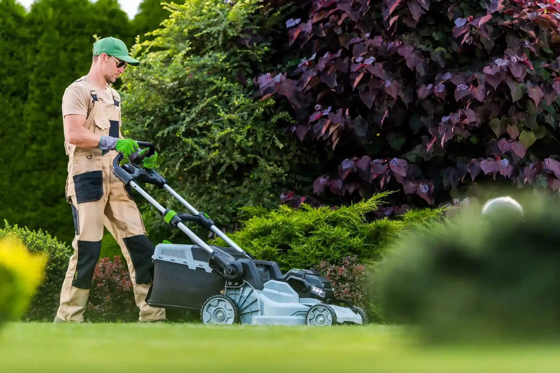 Professional landscaper mowing a lawn with trees and bushes.