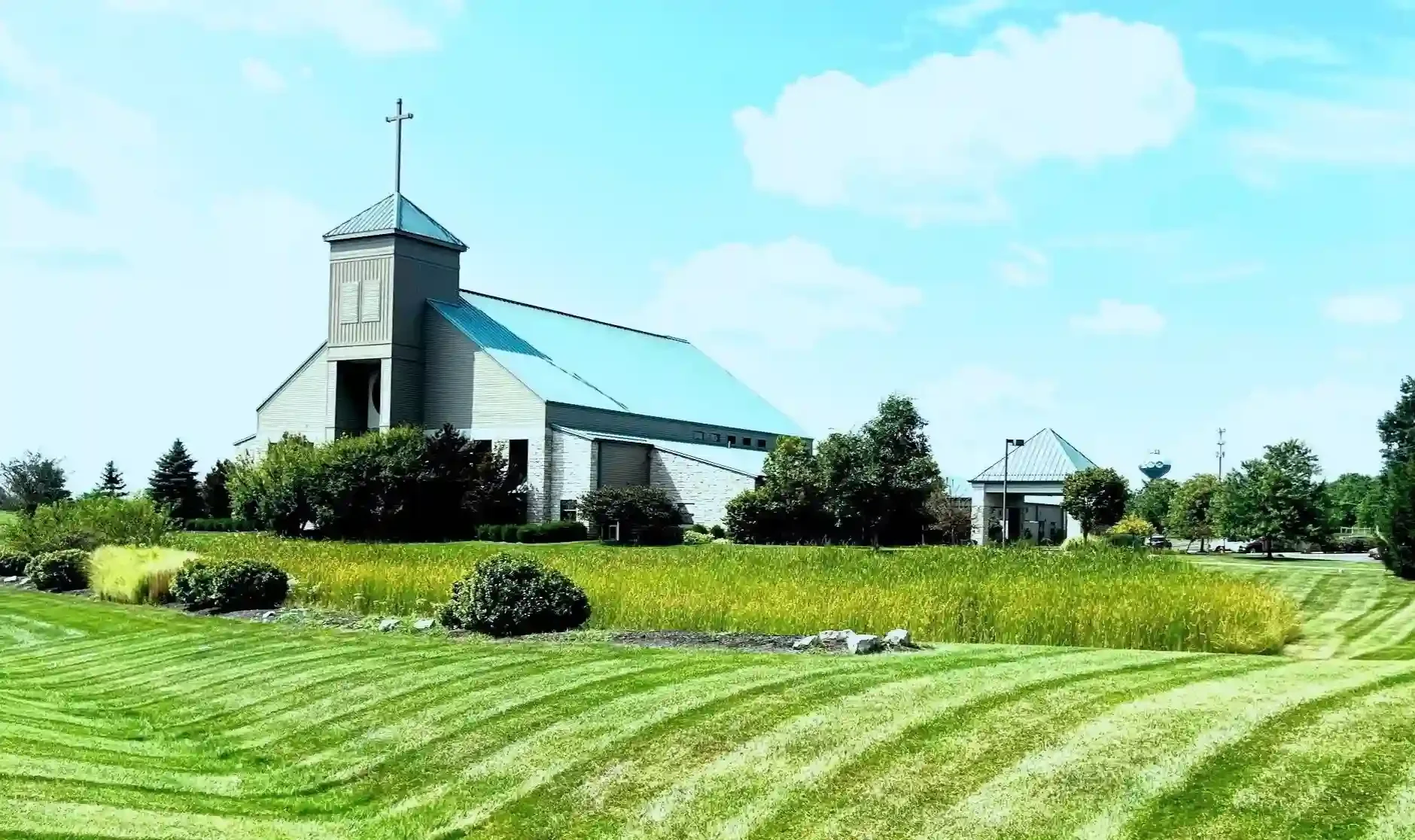 Professionally mowed lawn in the foreground of a church in front of a blue, cloudy sky.
