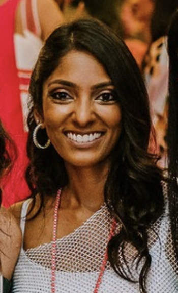 Smiling woman wearing a mesh top and hoop earrings at an event.