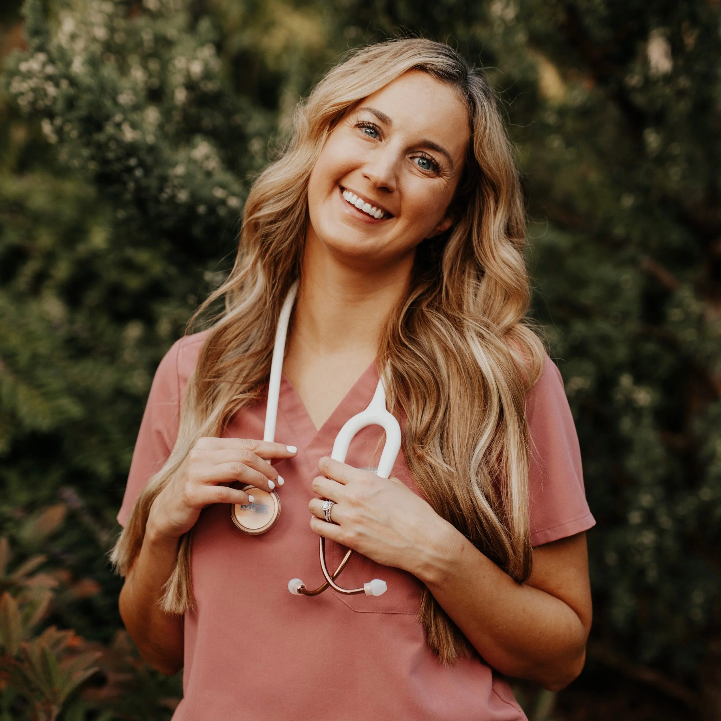 Smiling person wearing pink scrubs and a stethoscope outdoors
