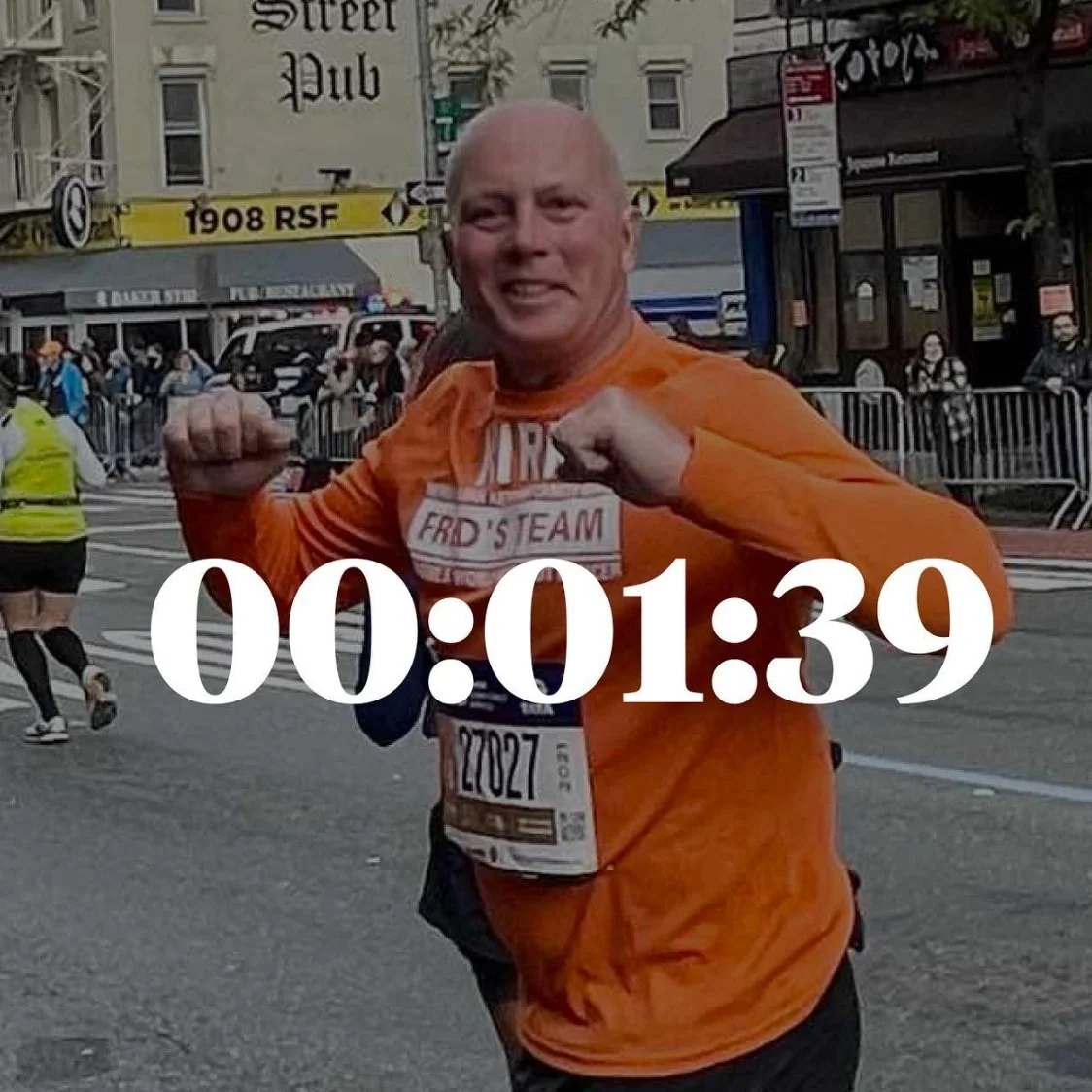 Runner in orange shirt during a race, smiling and posing with arms raised, number bib visible. Timer reading 00:01:39 overlays the image. Other runners and spectators in the background.