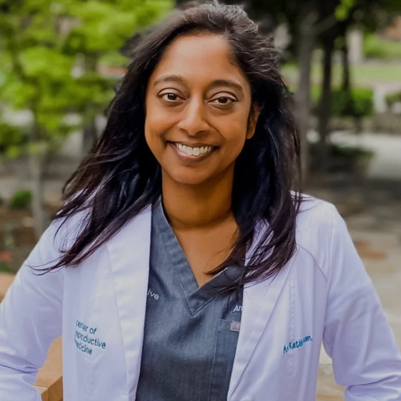 Smiling individual in medical scrubs and white coat outdoors