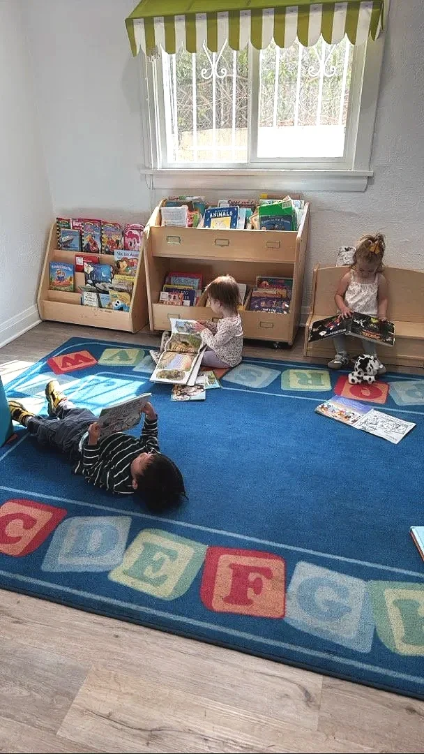 Children laying and sitting reading a book  at Chandlers Preschool in Highland Park, Ca. 