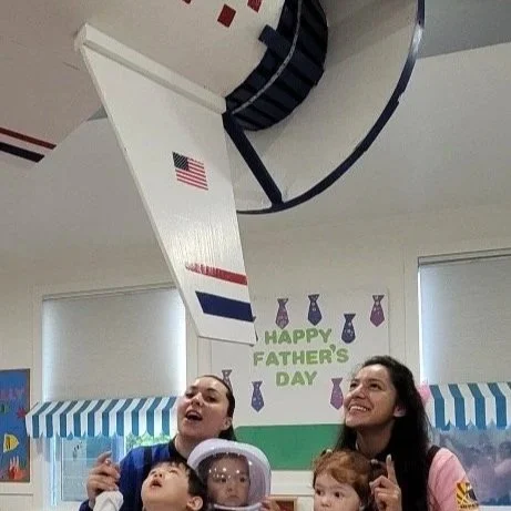 Children observing a space shuttle launch display in a classroom, exploring astronomy and science through hands-on, play-based learning activities.