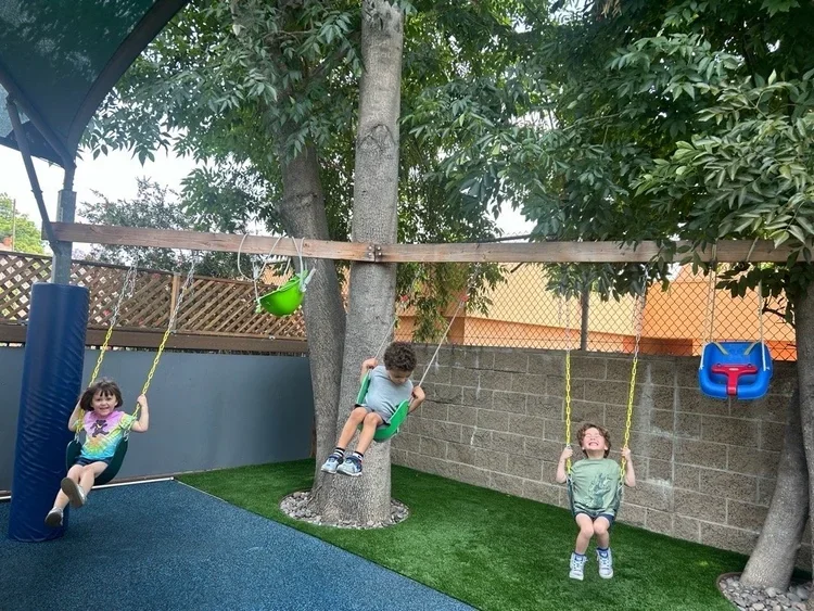 Childrenhaving fun on the  swingi set  in the playground at Chandlers Preschool