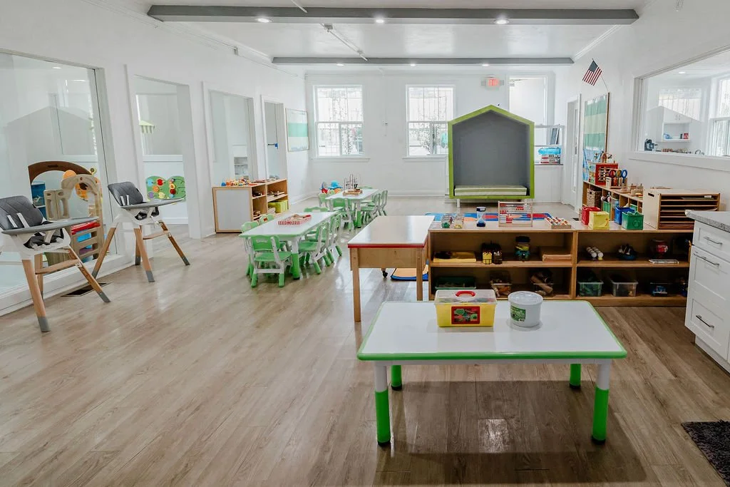 Bright and spacious preschool classroom with small tables, chairs, toy storage, and play areas for young children.